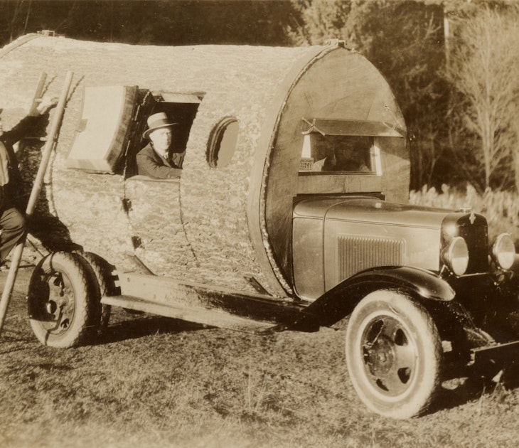 Two men driving log cabin RV circa 1915