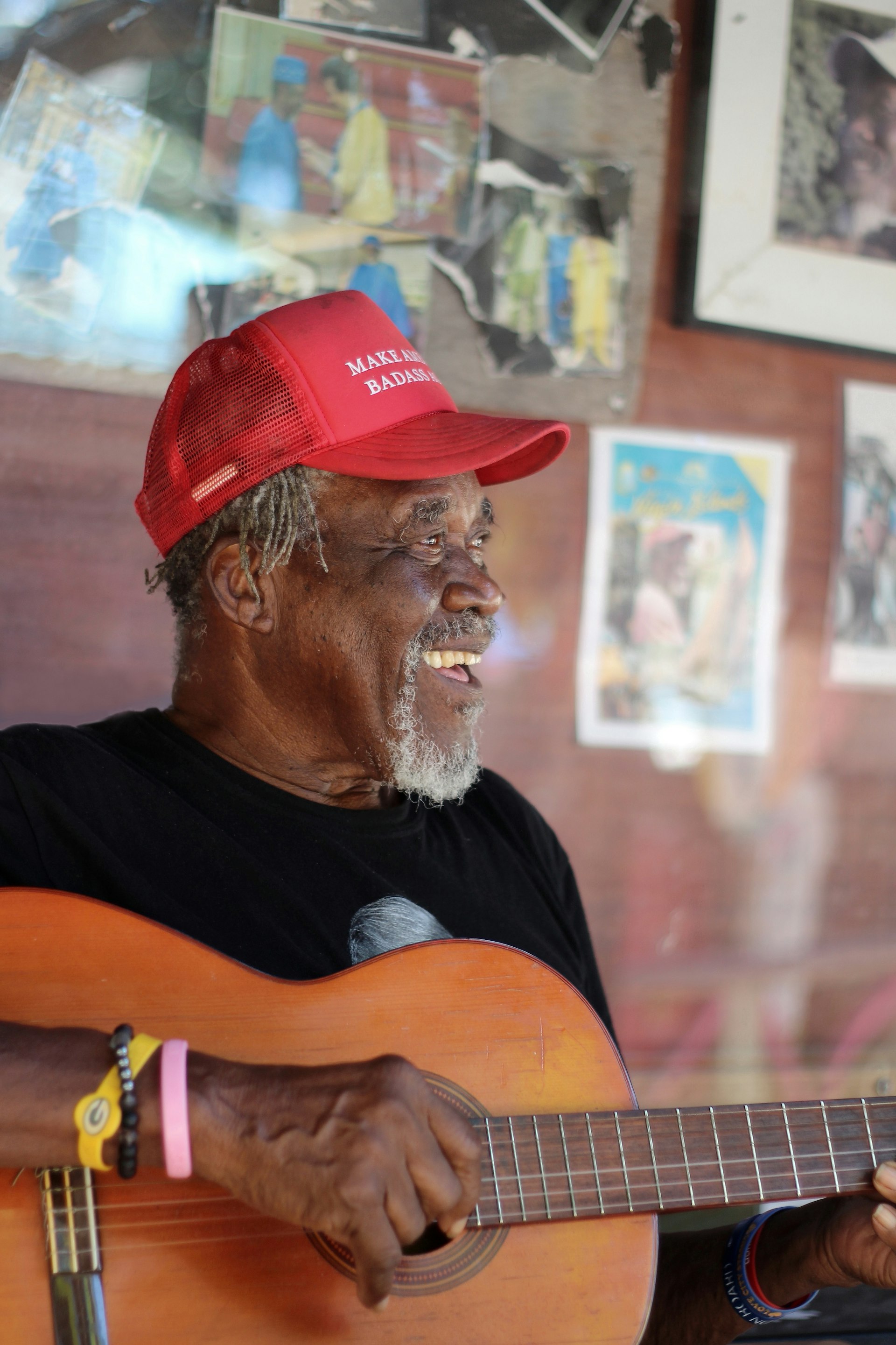 A man, wearing a red cap, strums on a guitar and sings