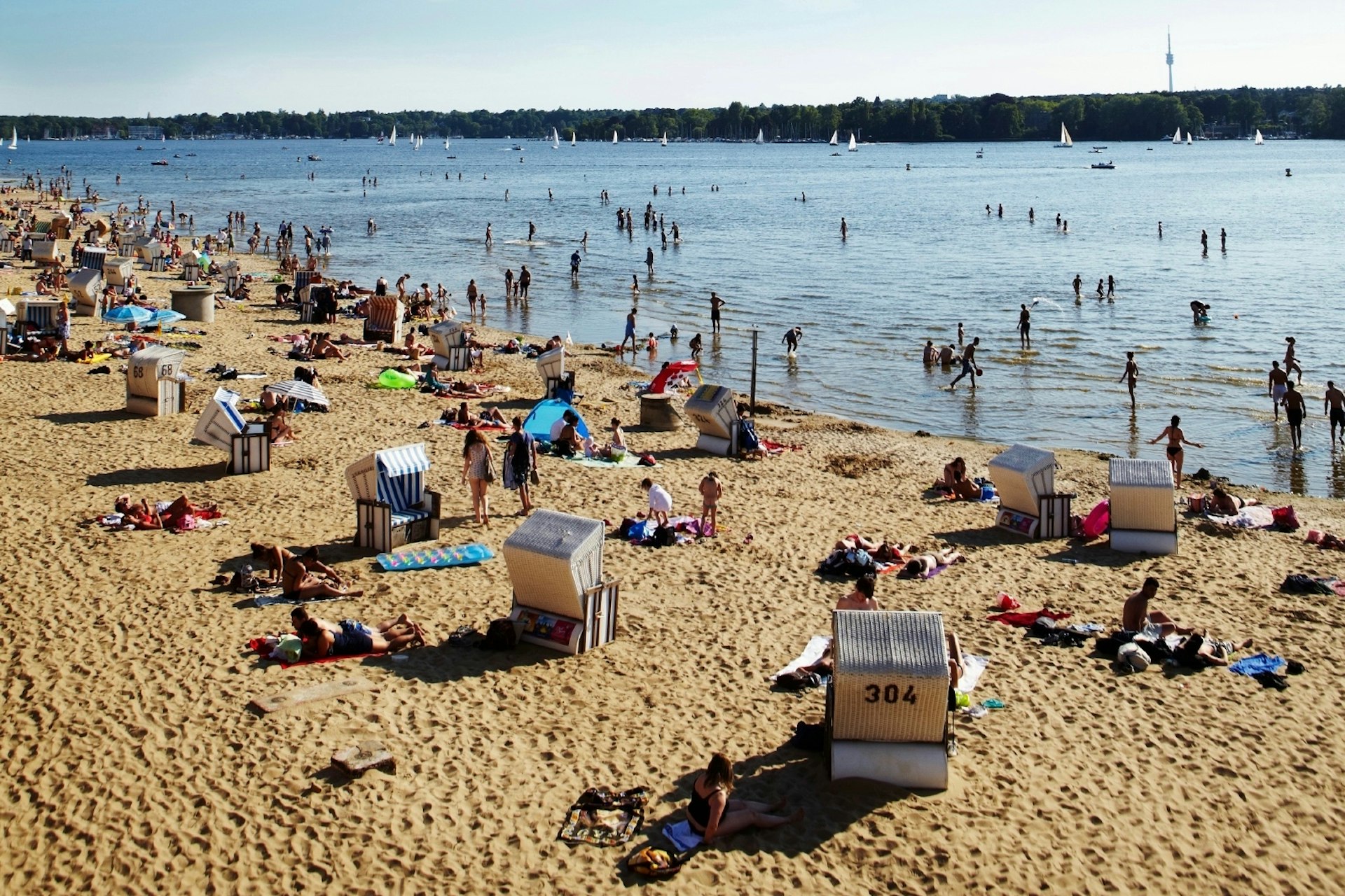 A sandy beach by a lake. People are lying on the beach and playing in the water.