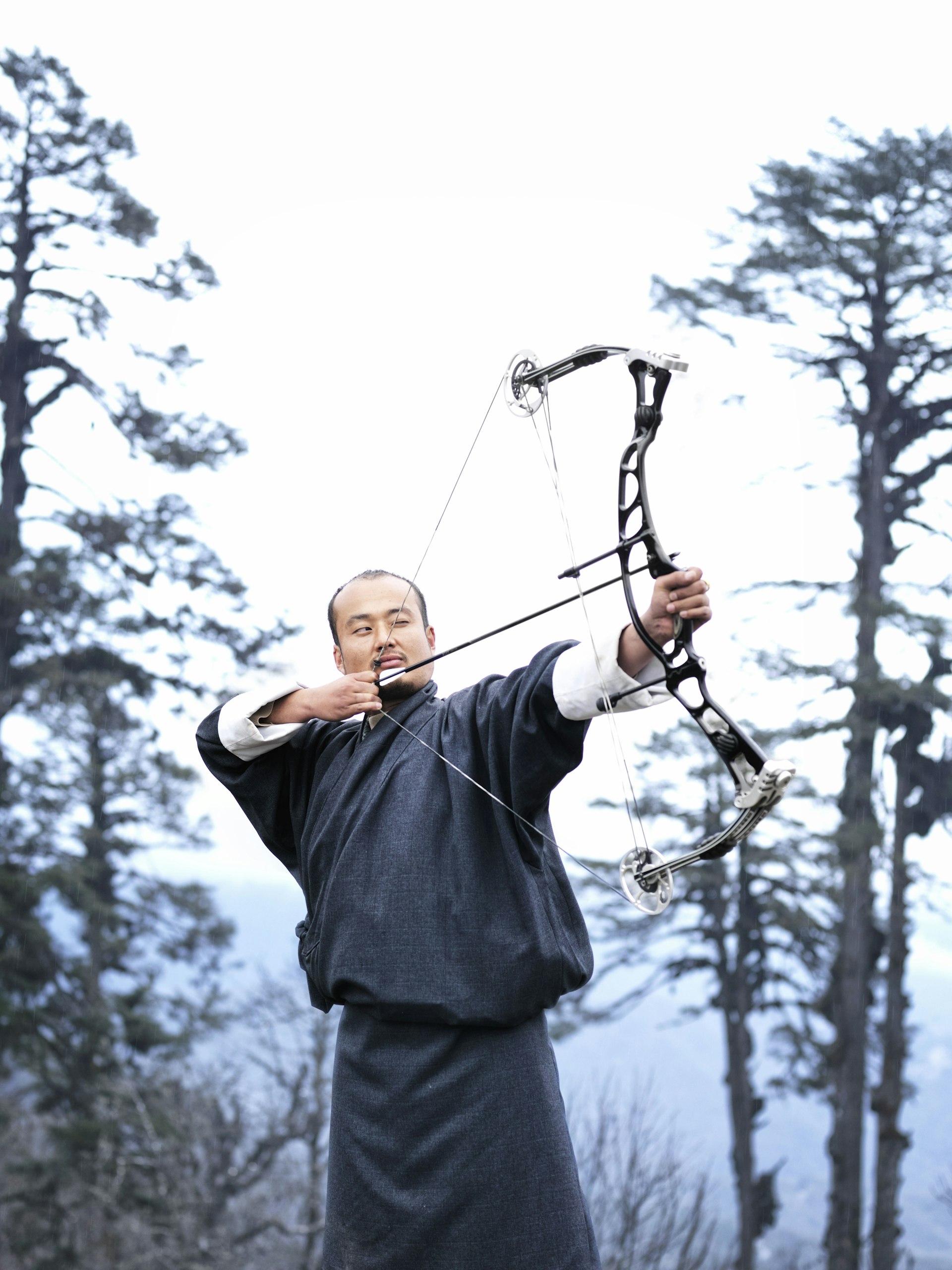 A man dressed in black stretches back his bow and aims an arrow into the distance