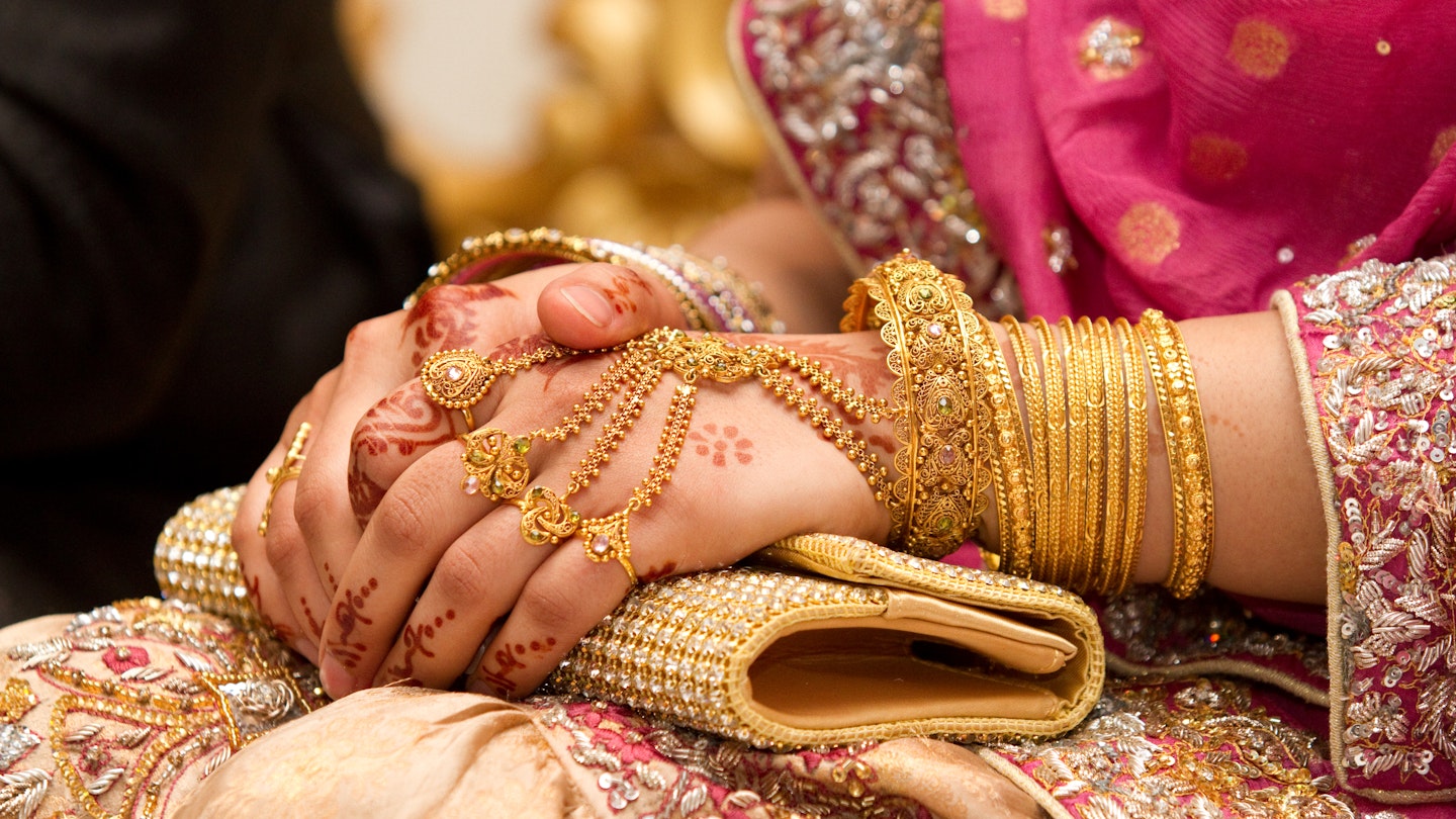 Muslim brides hands decorated with henna and gold jewellery.