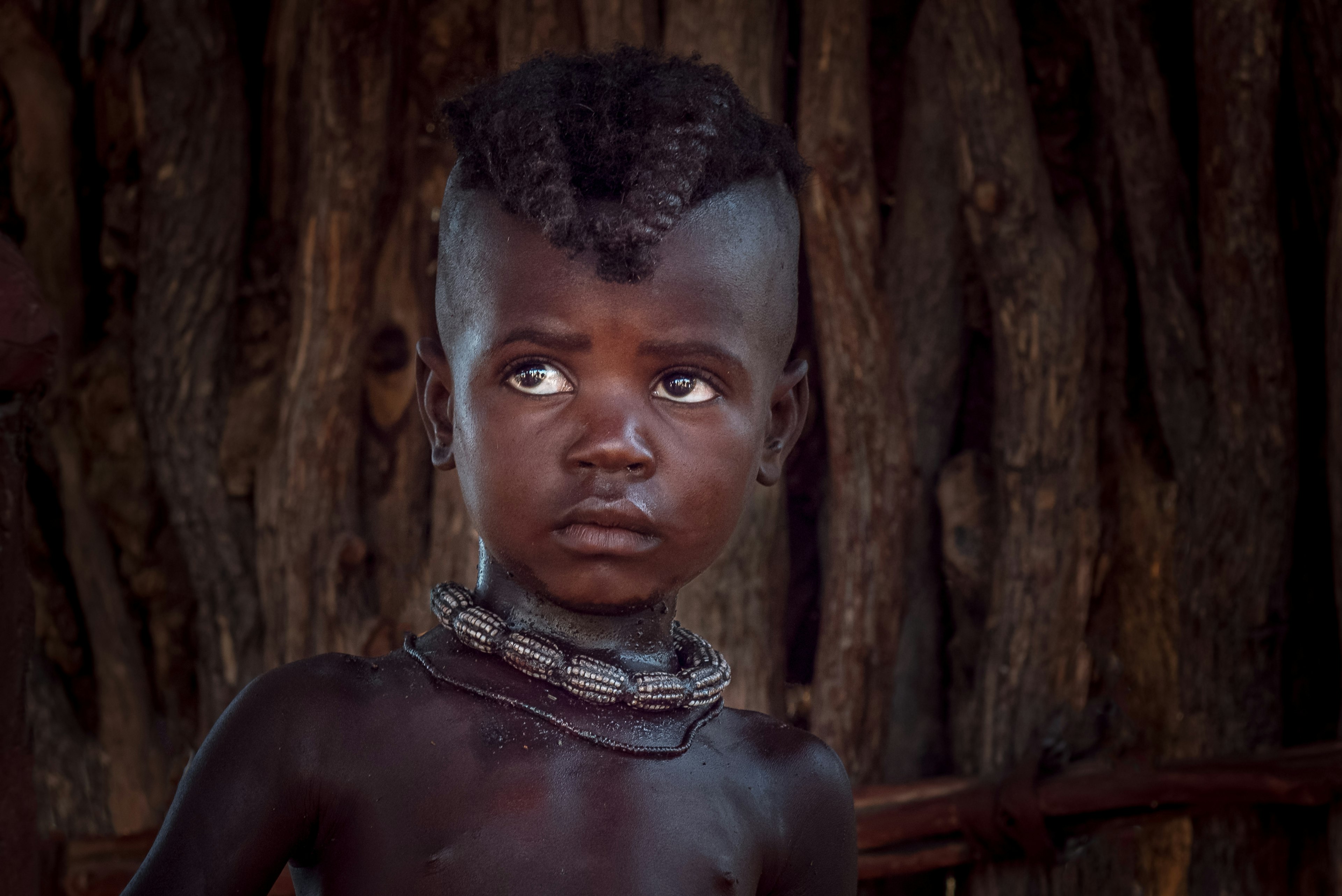 A close-up shot of a young child wearing two beaded necklaces and with hair styled in plaits coming over they're forehead