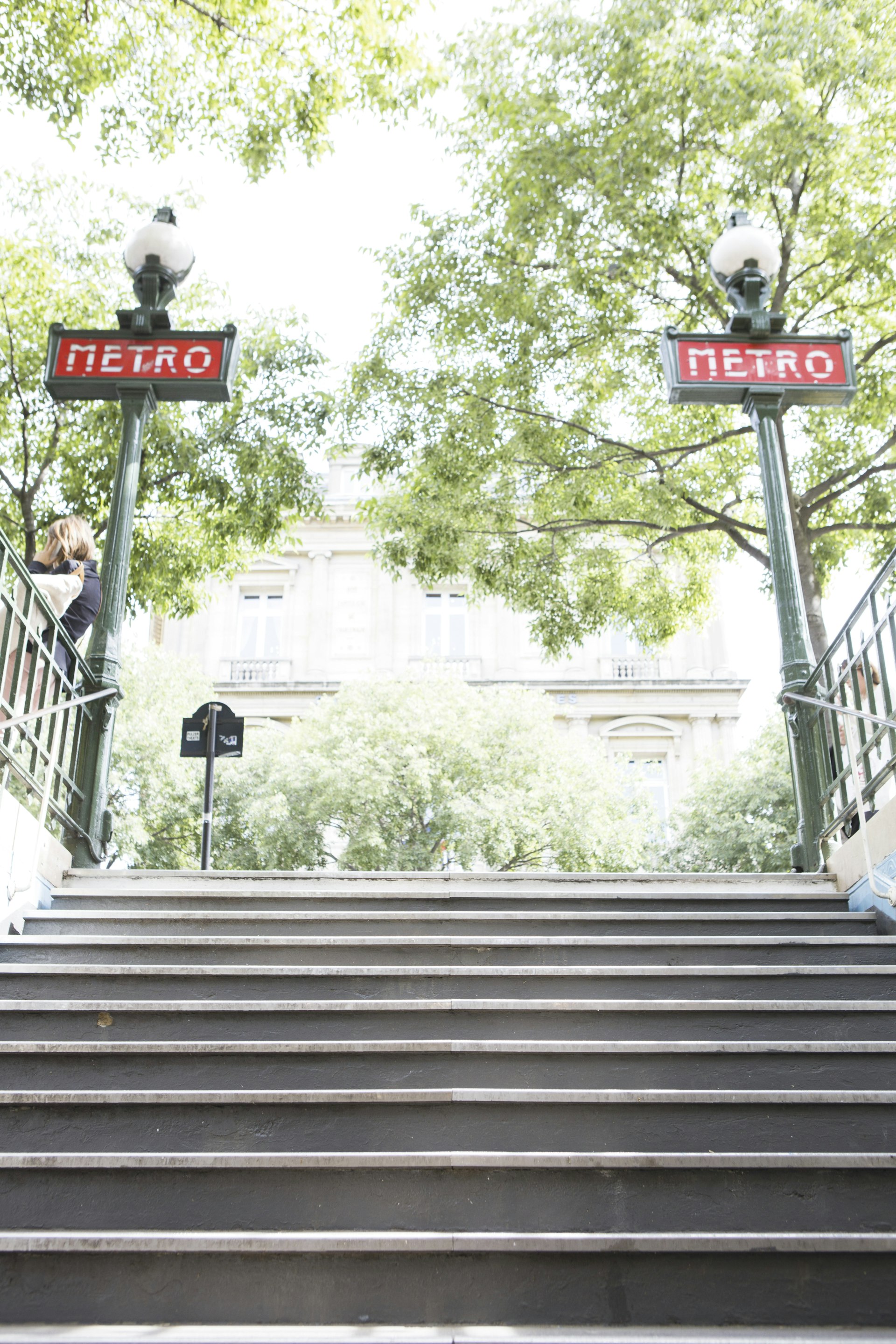 A shot up a flight of stairs coming out of an underground station. Two red-and-white signs at the top say "metro"