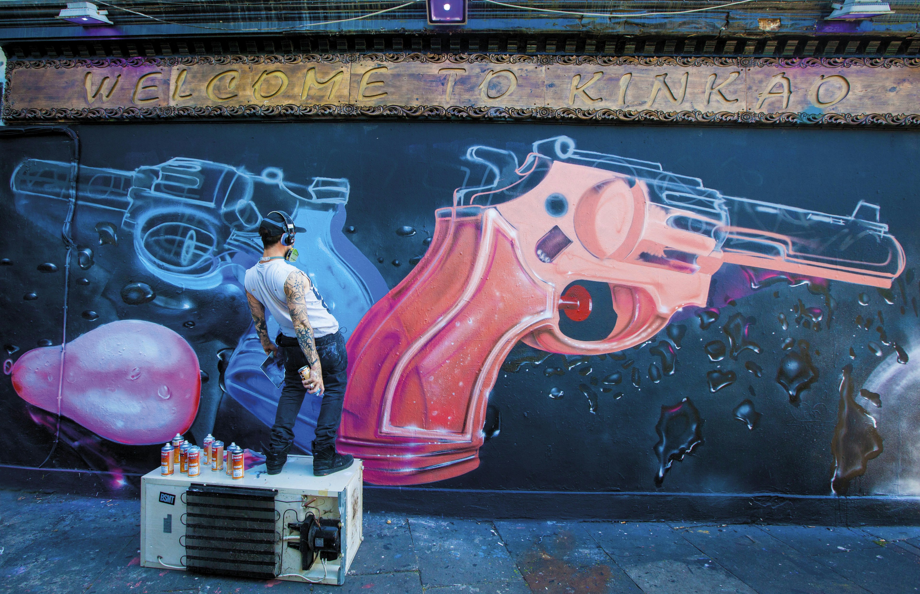 A street artist spray paints two colourful guns onto the wall of Kinkao Korean, in Shoreditch.