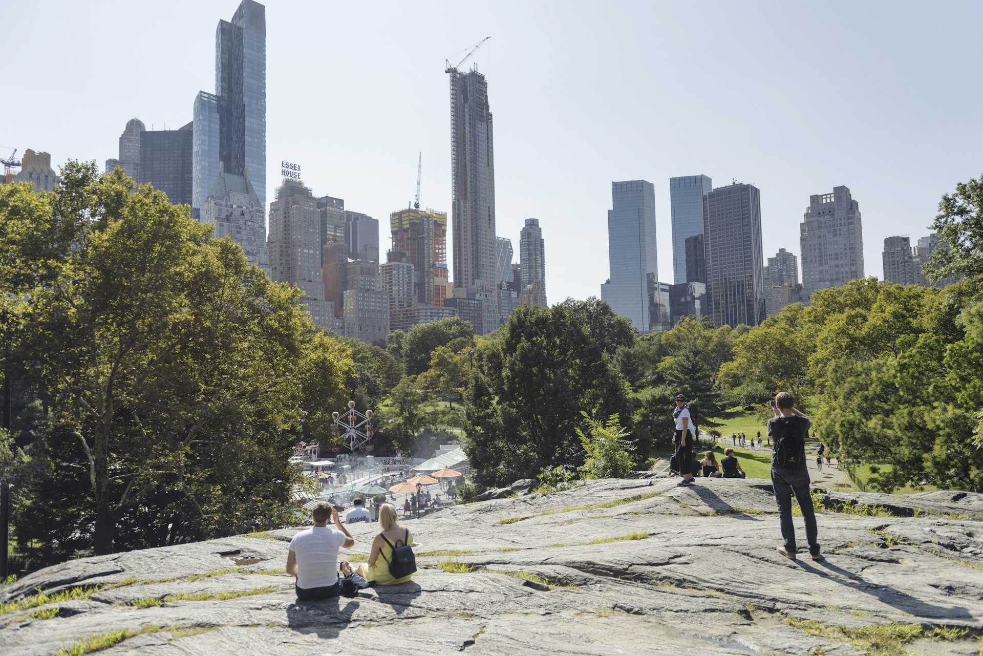 People relax on a rocky section of Central Park, with Victorian Gardens Amusement Park in the distance.