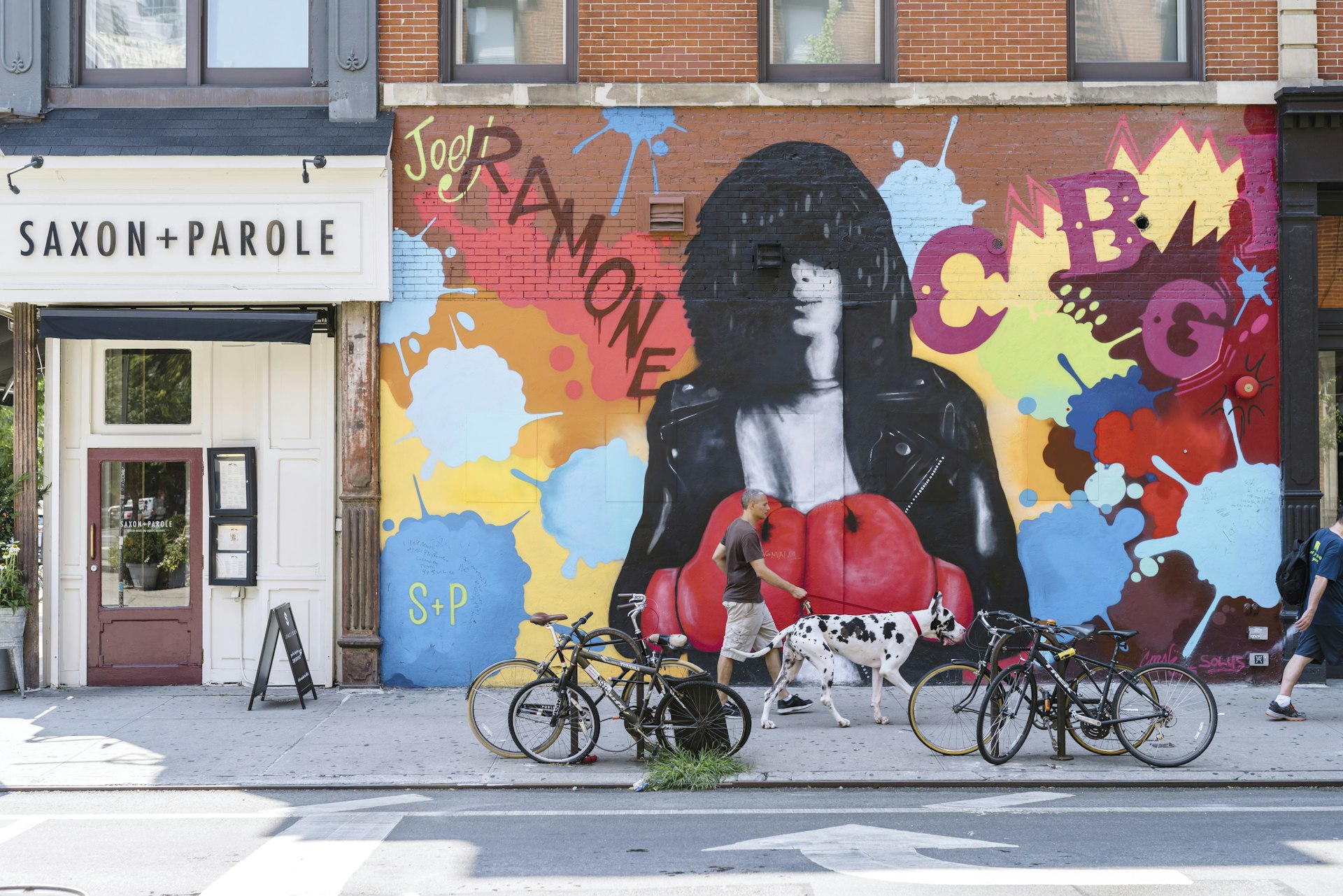 A man walks his dog in front of street art at the corner of Bleecker and Bowery. 