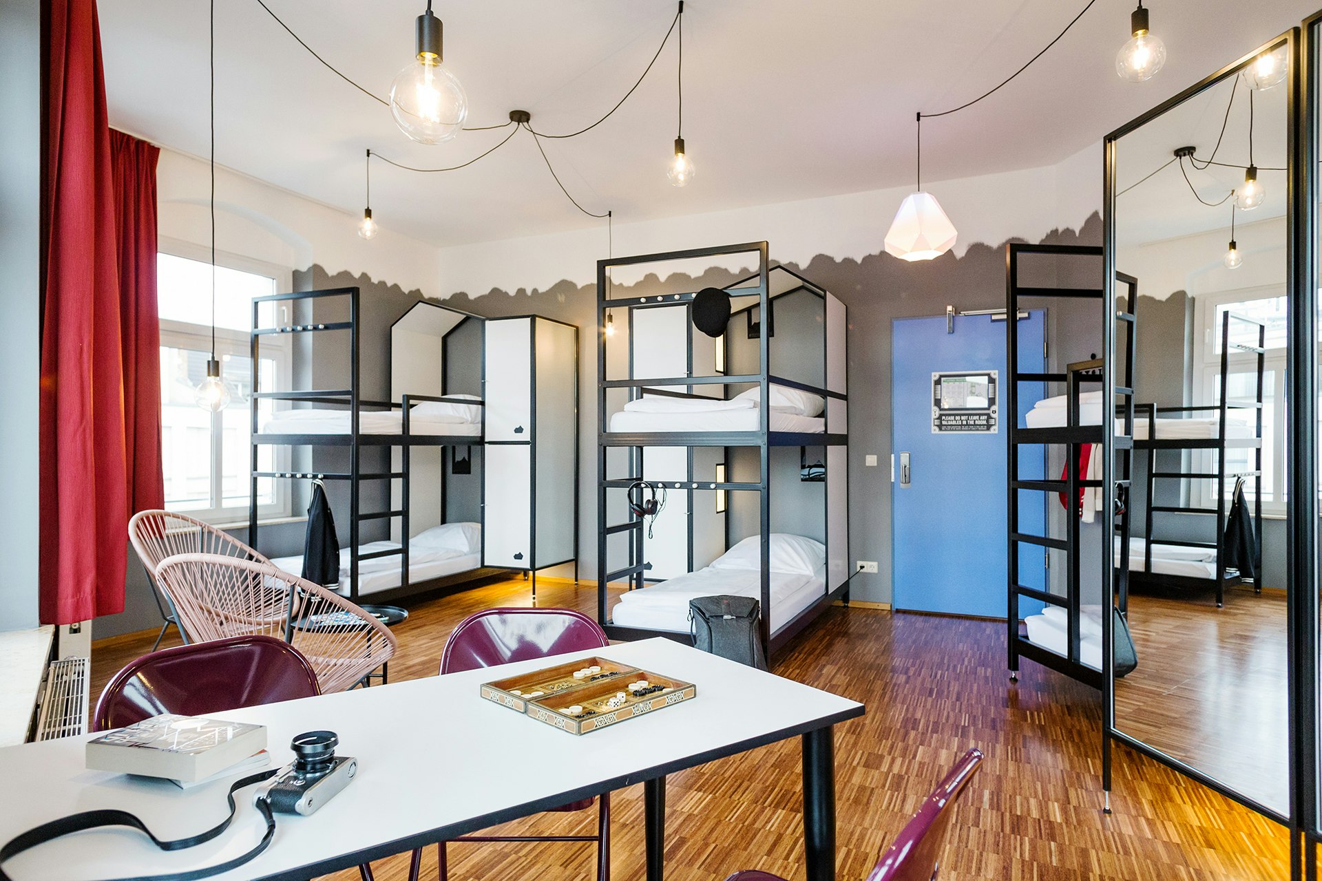 A spacious dorm room, with stylish black-and-white bunks, white bed linen, a table and several chairs 