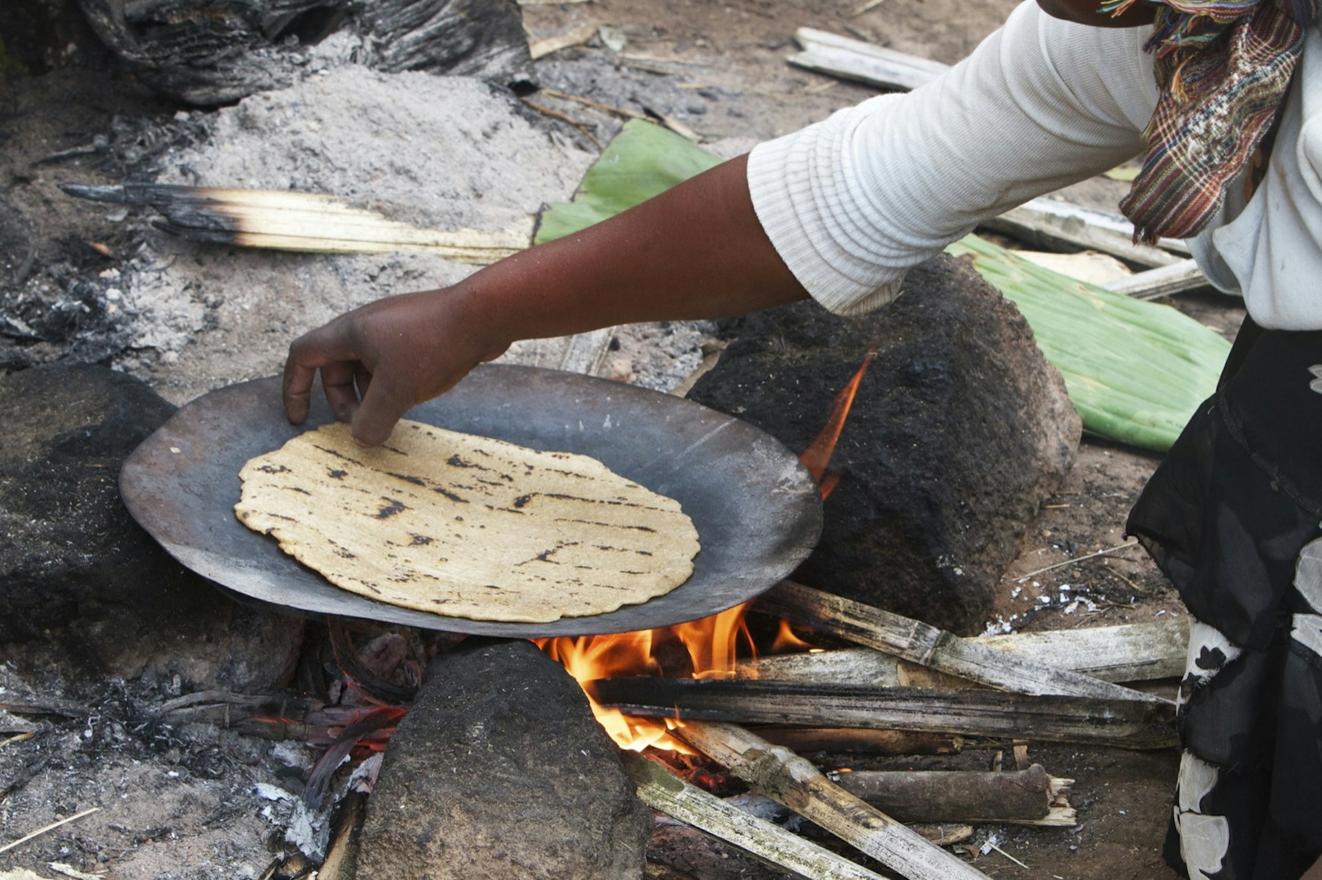 Person prepares injera on a flat pan over an open flame