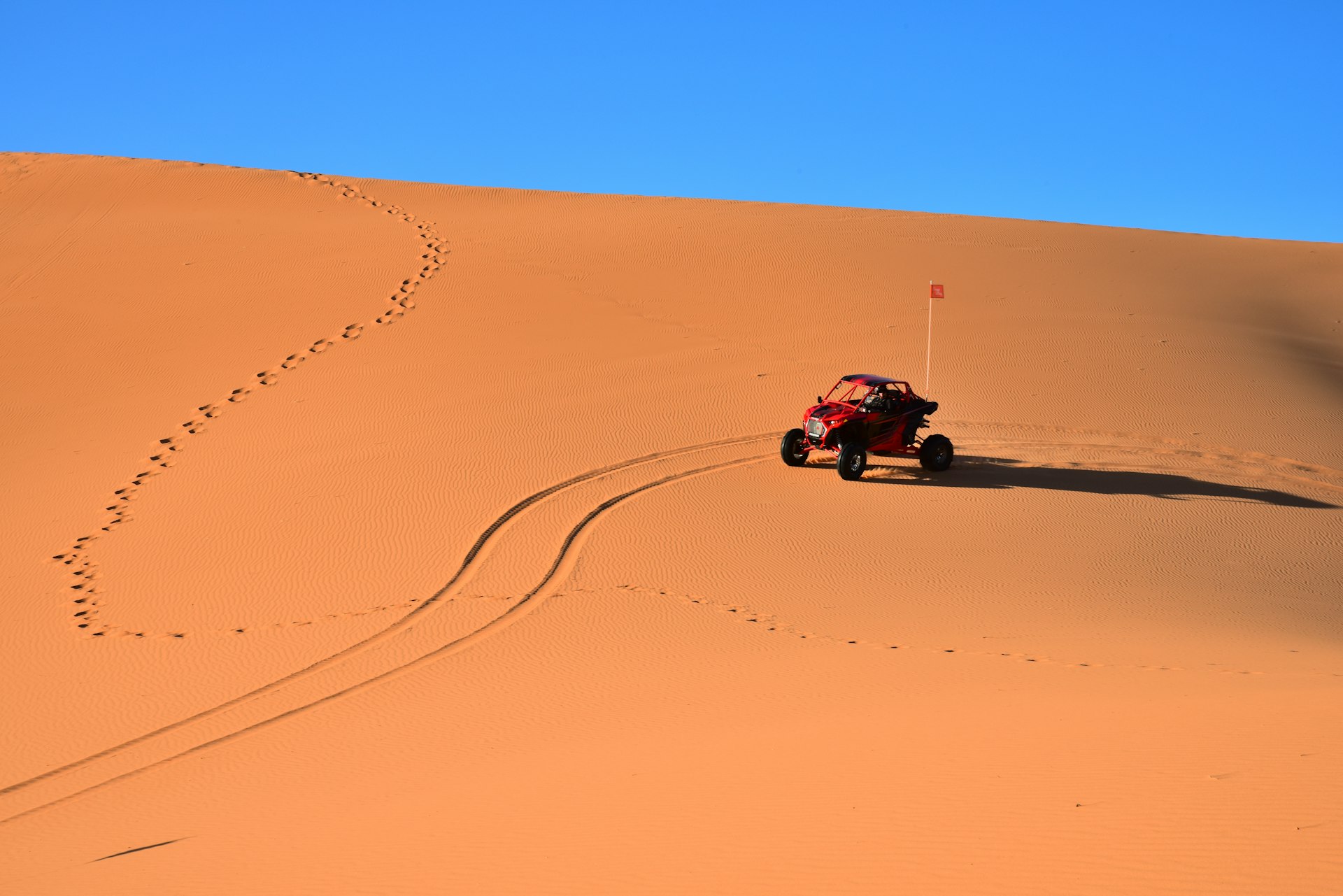 An all terrain vehicle slides down an orange-pink colored sand dune