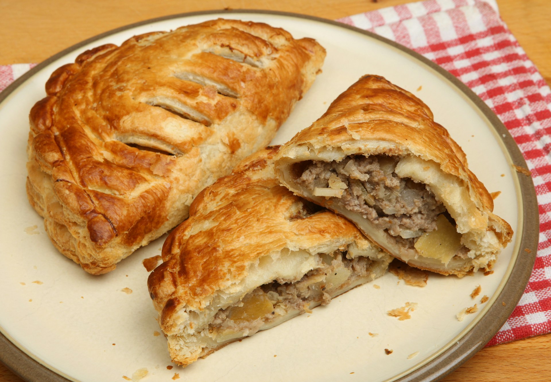 Freshly baked Cornish pasties on a plate. The pasty has been cut in half, revealing its meaty content that's wrapped in baked pastry. 