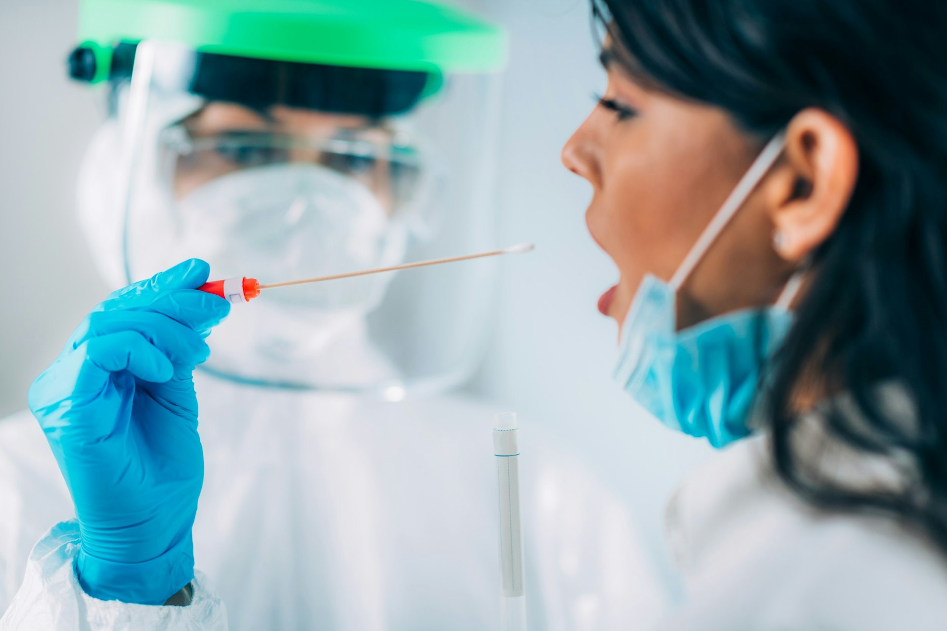 A medical worker in a protective suit taking a swab for coronavirus from a young woman