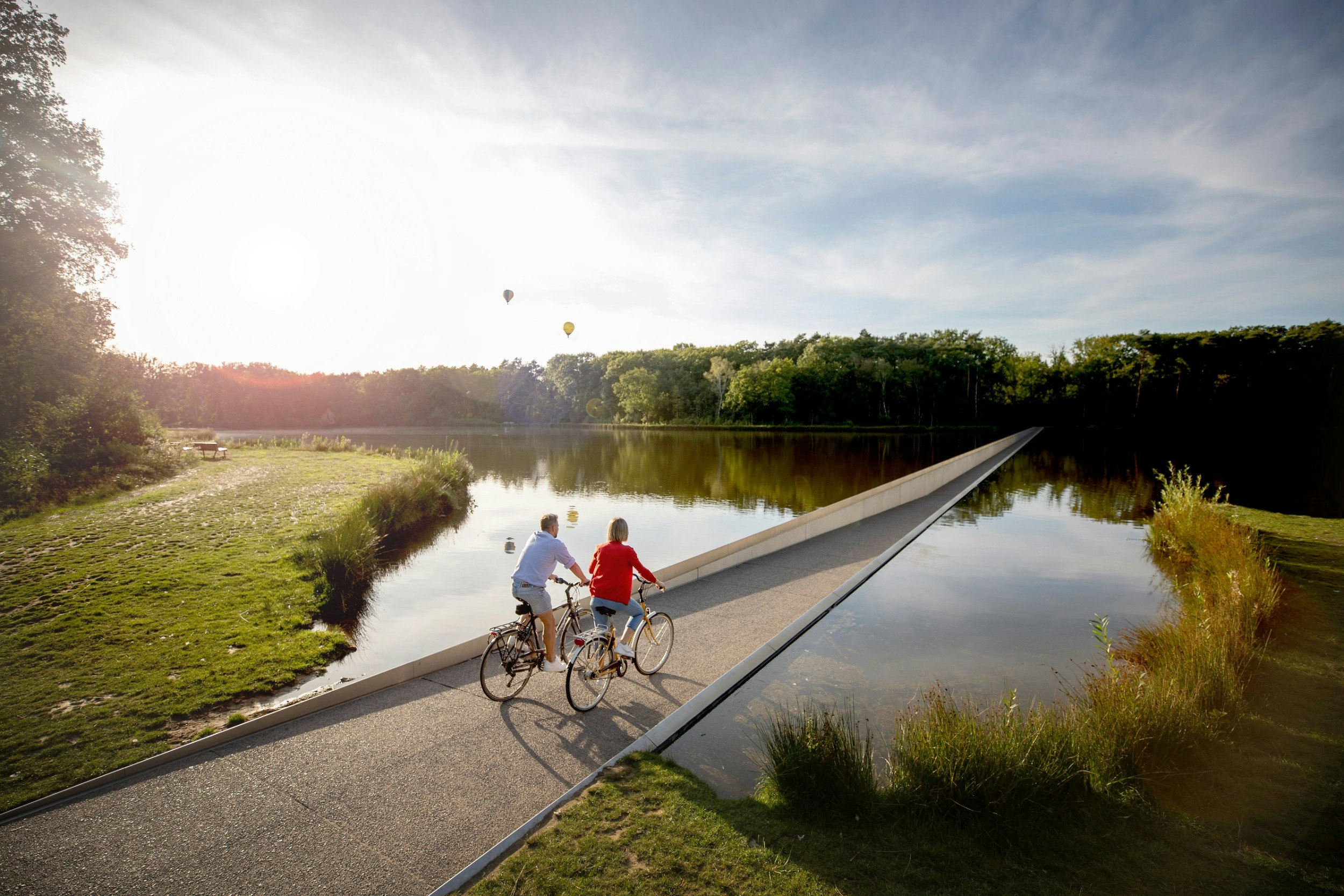 Two people cycling on a path through a pond