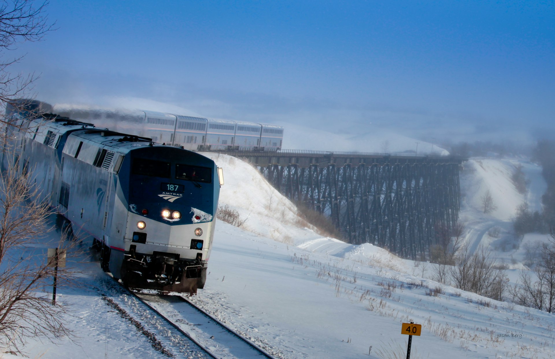 A large train coming over a trestle bridge in heavy snow