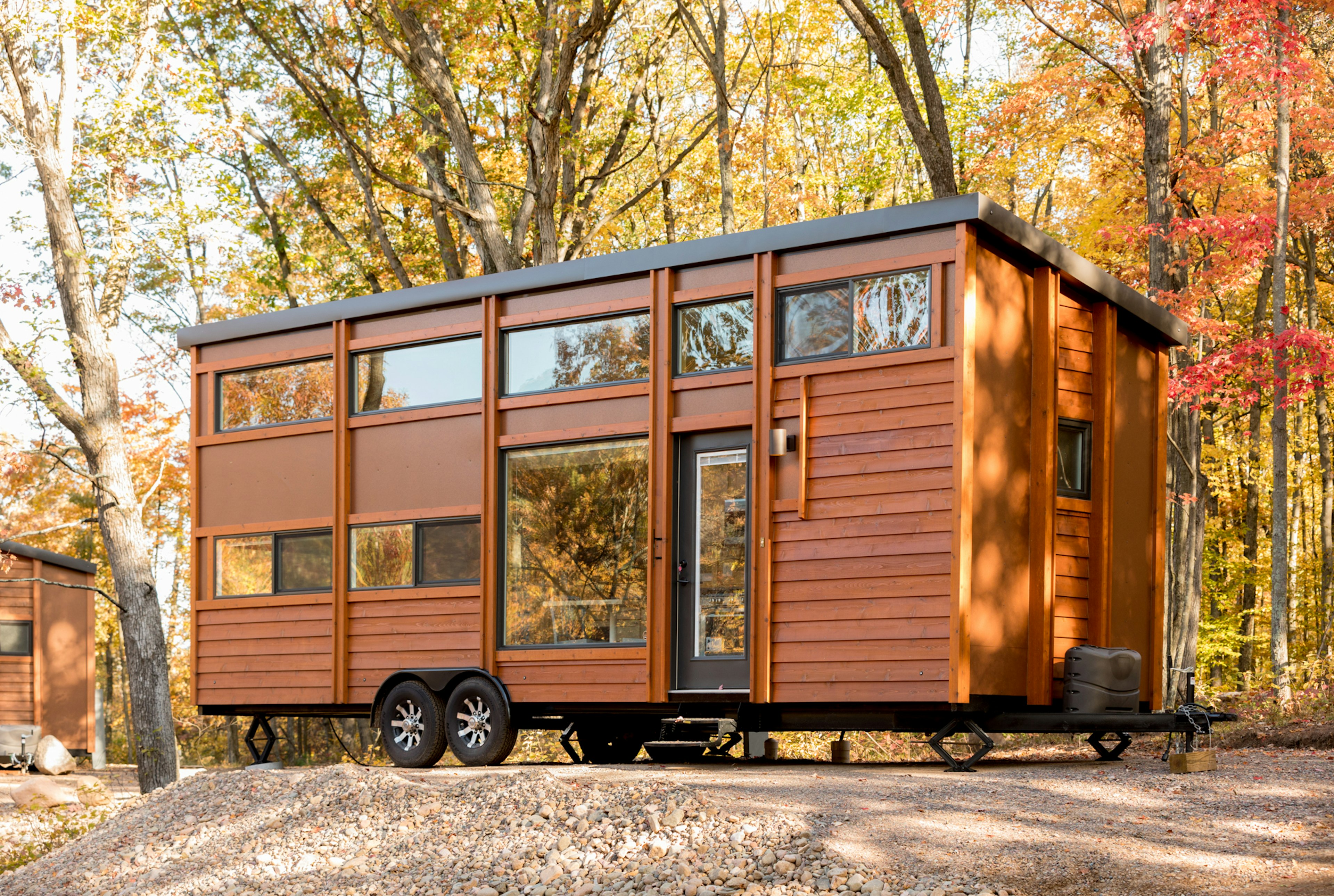 A large two-storey wooden cabin on wheels in a woodland setting