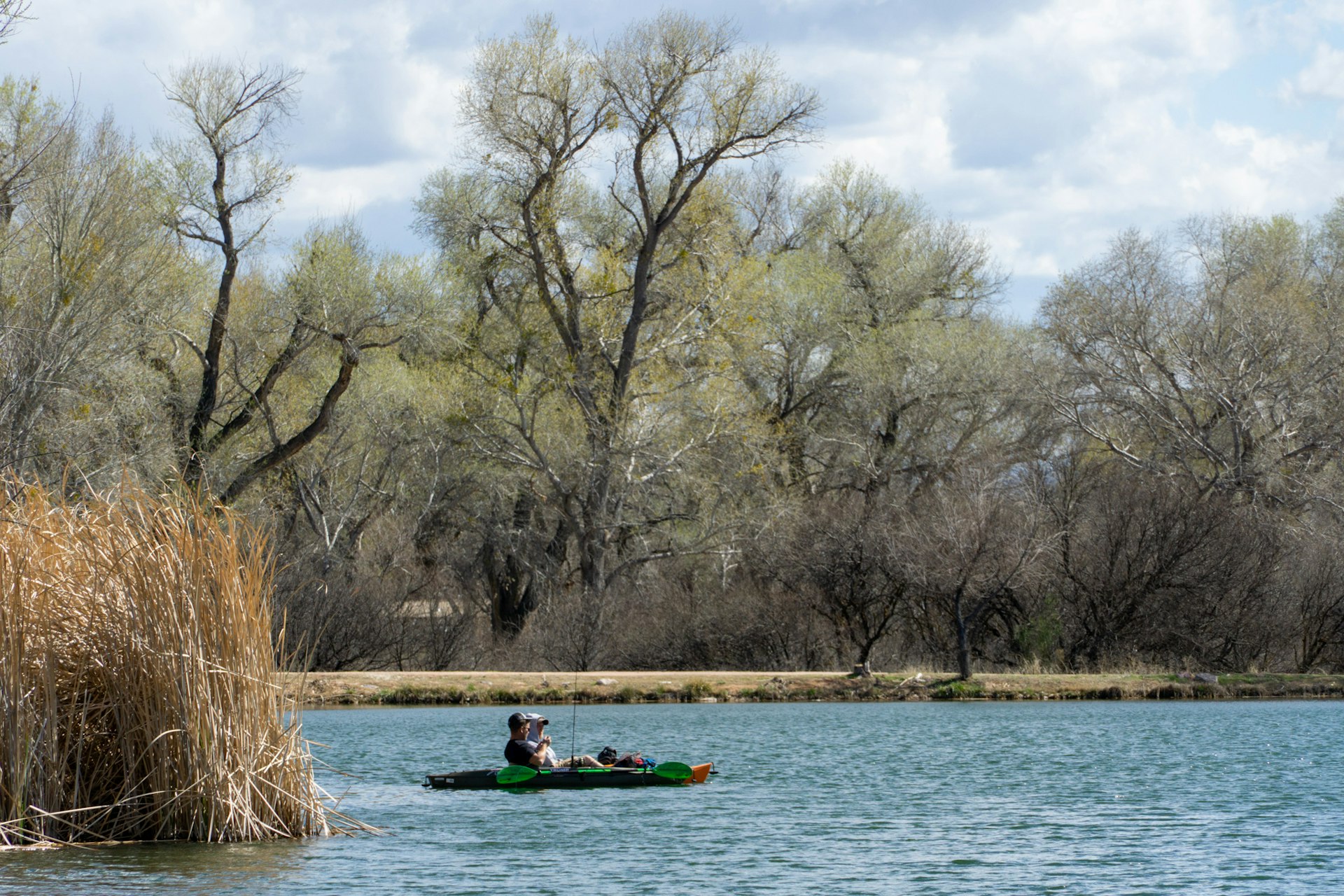 Two people with fishing rods sit on a kayak in a calm lake