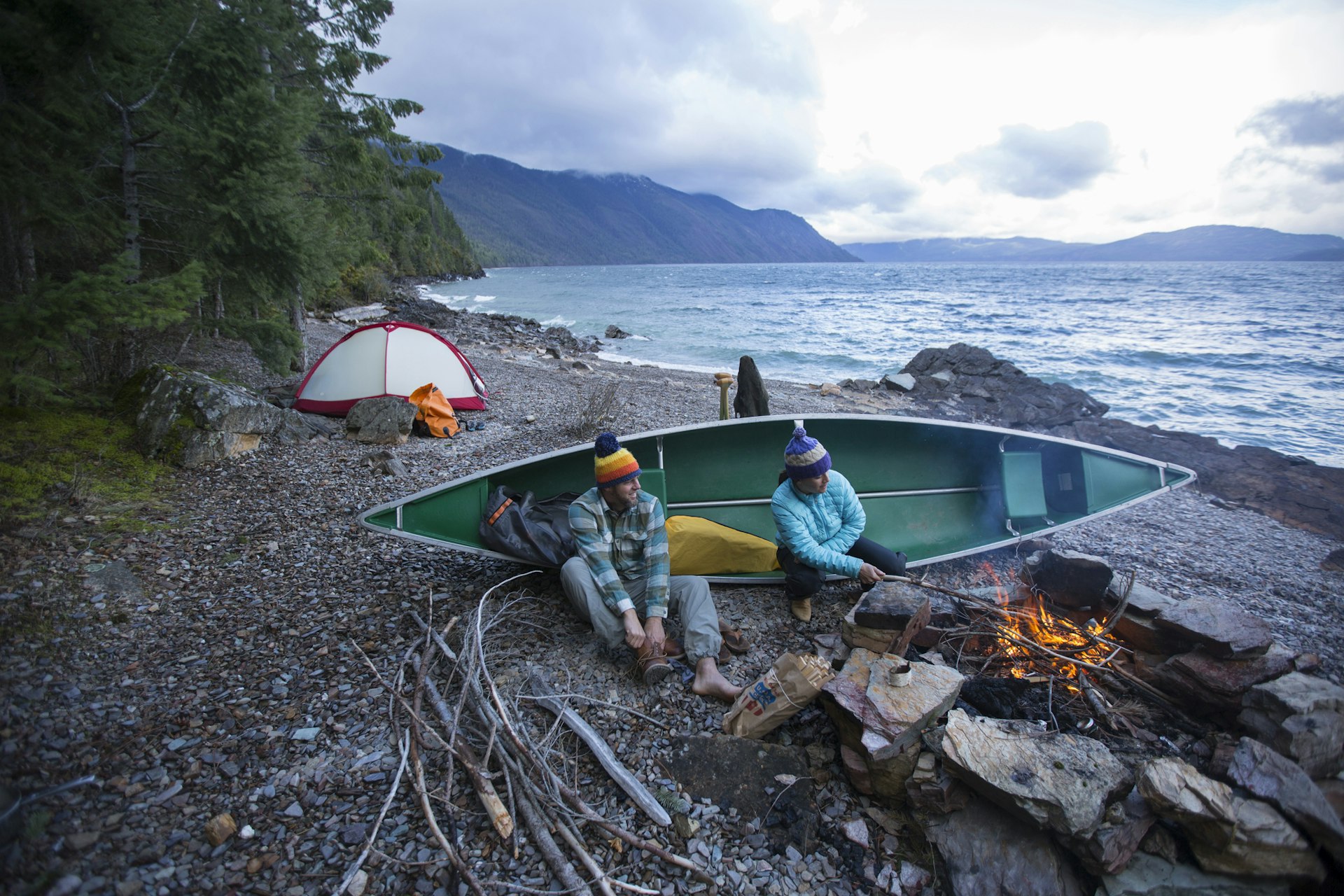 Couple sitting by campfire while canoe camping on Lake Pend Oreille.