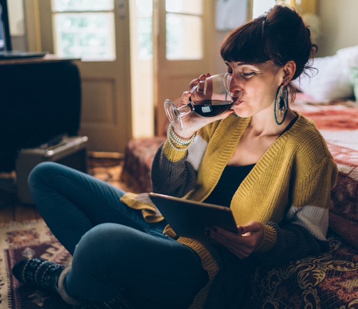 Young woman at home drinking red wine and using tablet