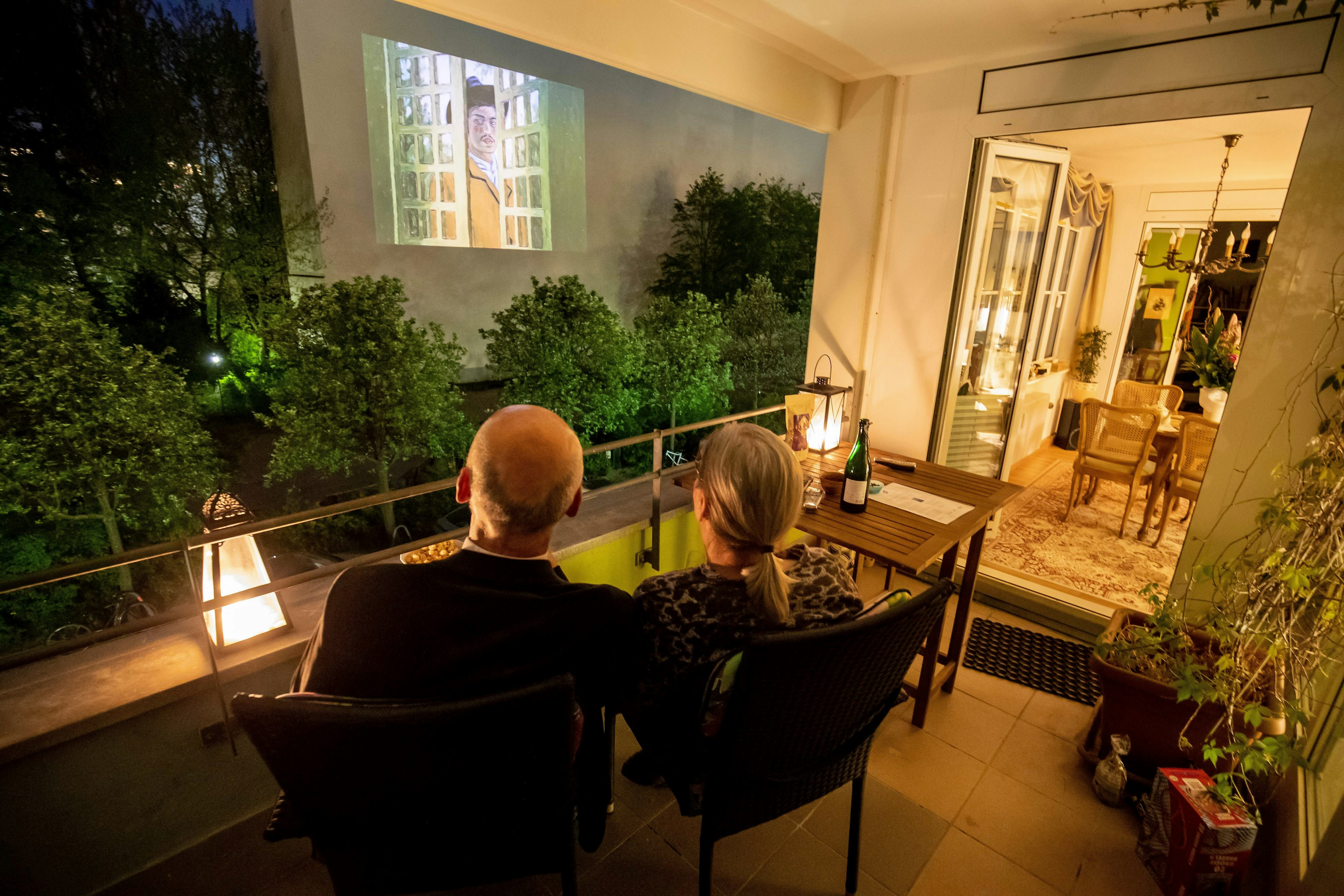 A family watch a movie projected on the wall of a neighbouring building from their balcony