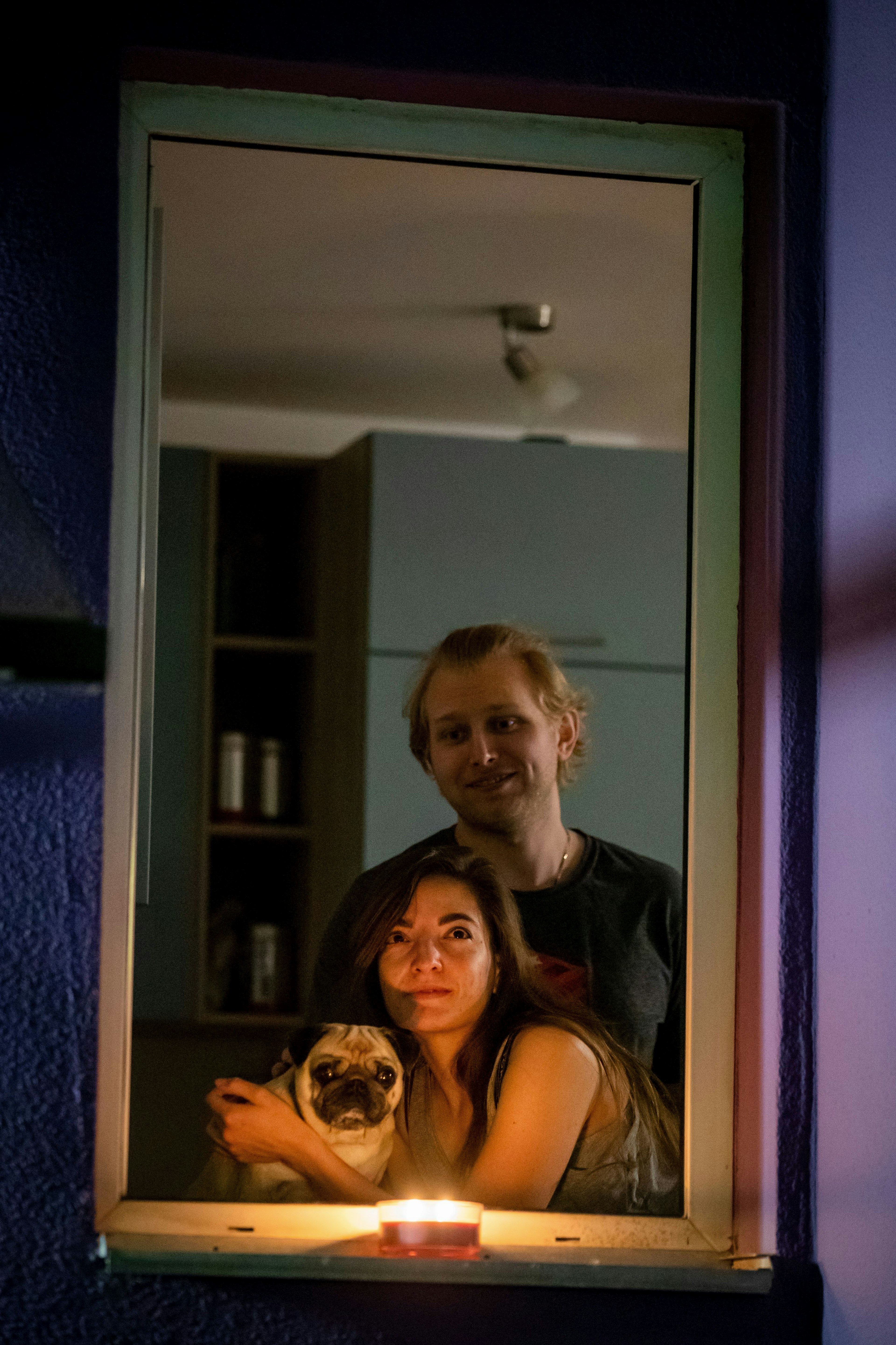 A couple and their pug watch a movie from the window of their apartment