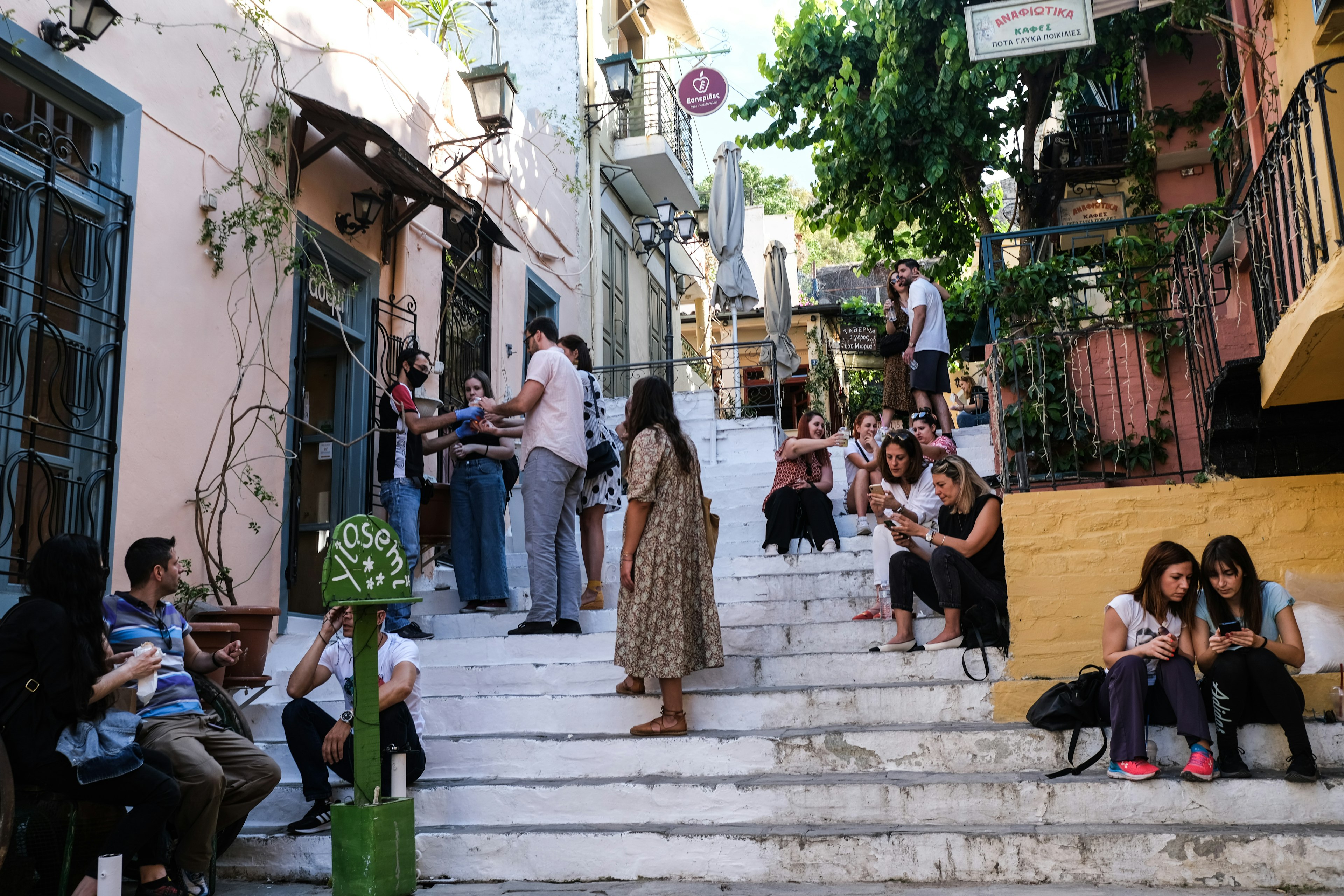 Tourists and locals mill about on white steps outside of a cafe on a hillside