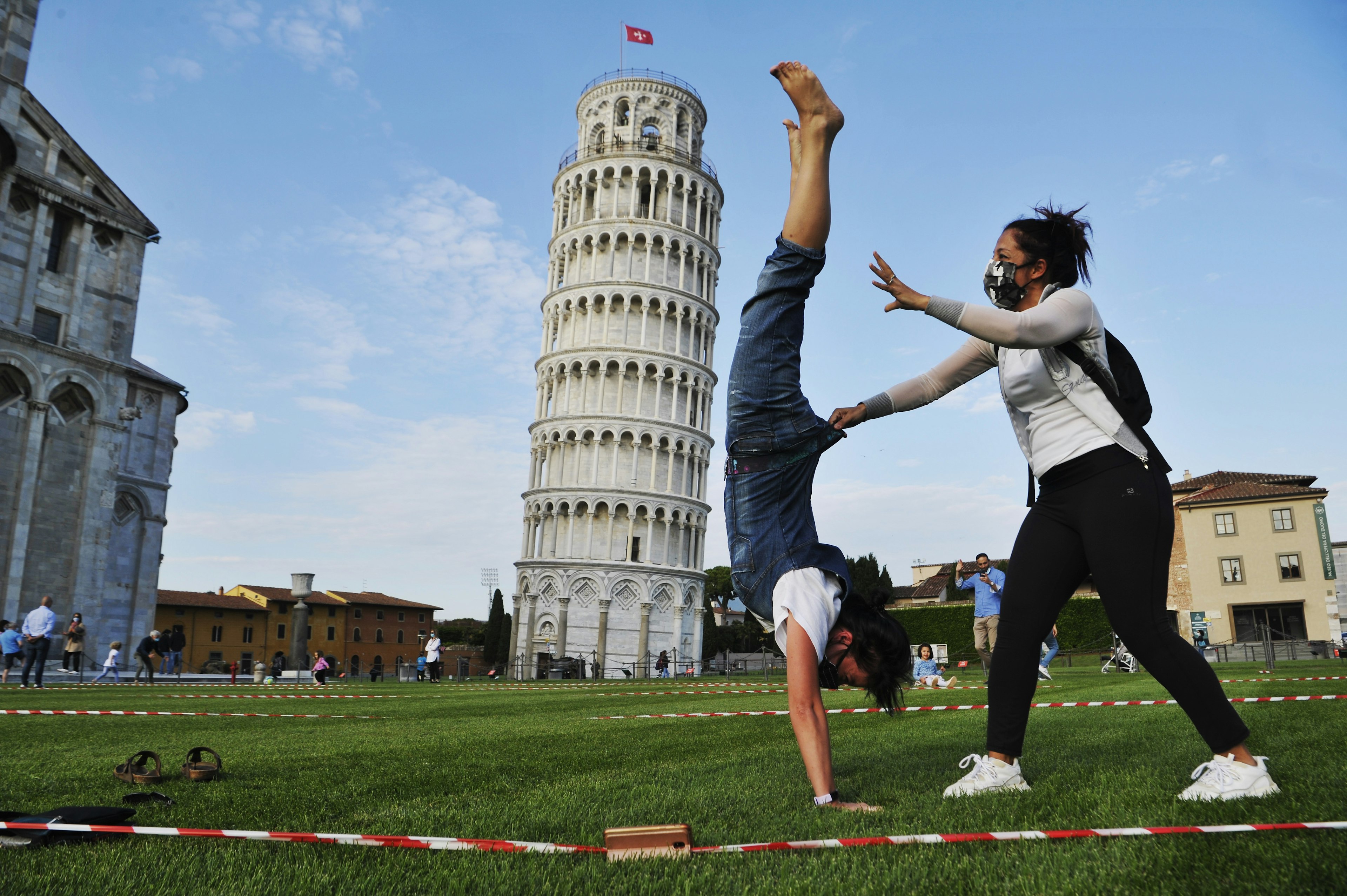 Tourists wearing face masks pose for a photograph near the tower of Pisa