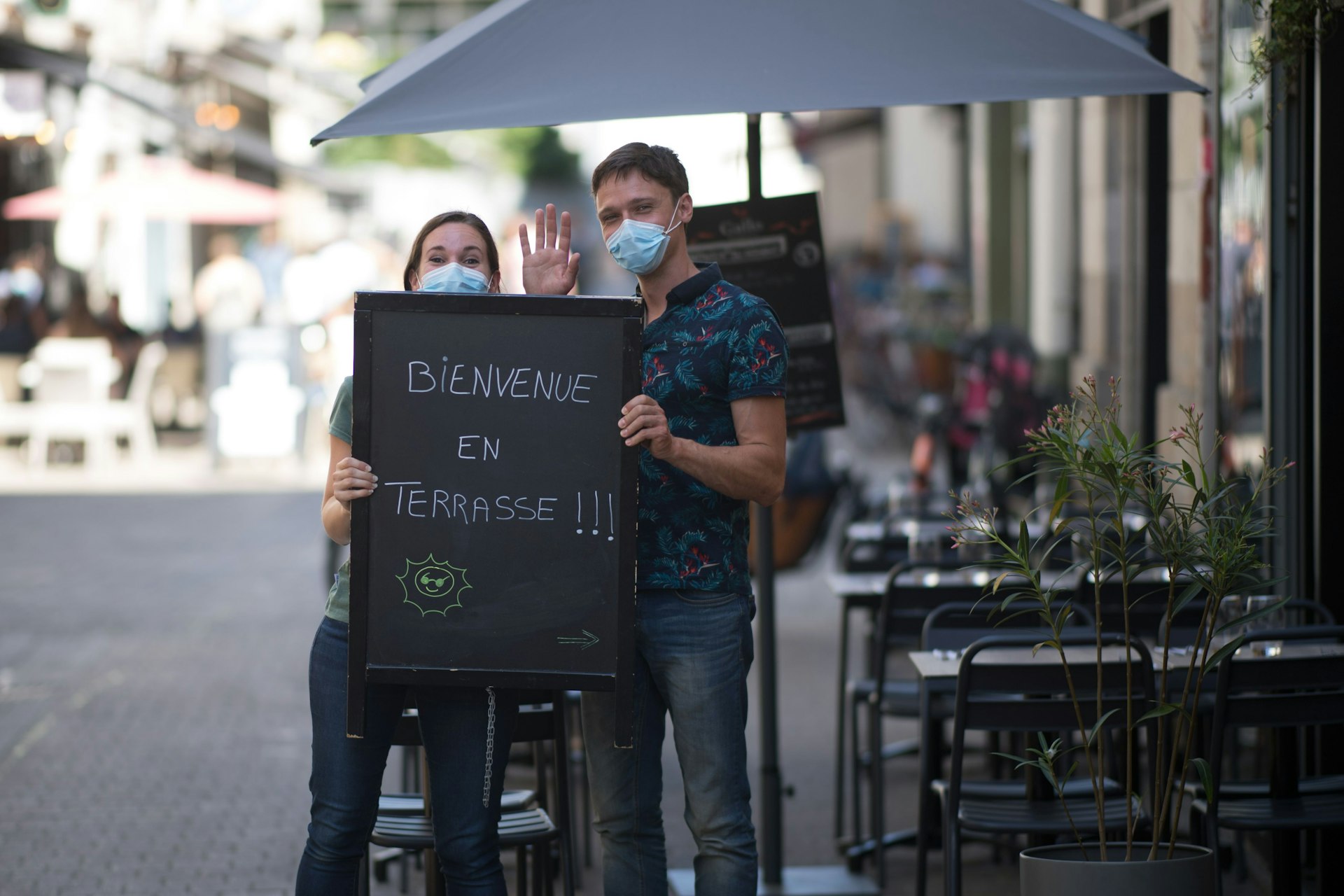 Waiters holds a black board reading " Welcome on terrace " outside a cafe terrace in Nantes