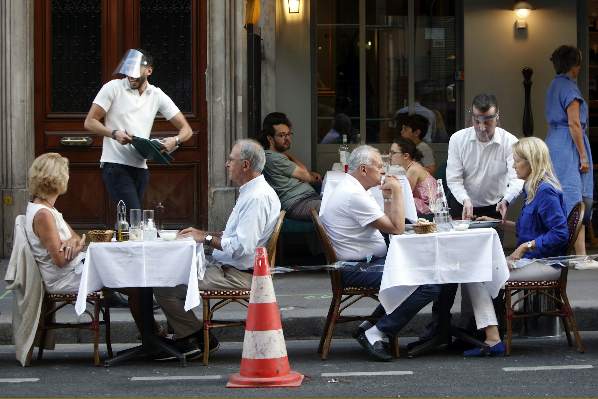 A waiter wearing a face mask serves clients while people eat and have drinks on the terrace of the cafe-restaurant in Paris