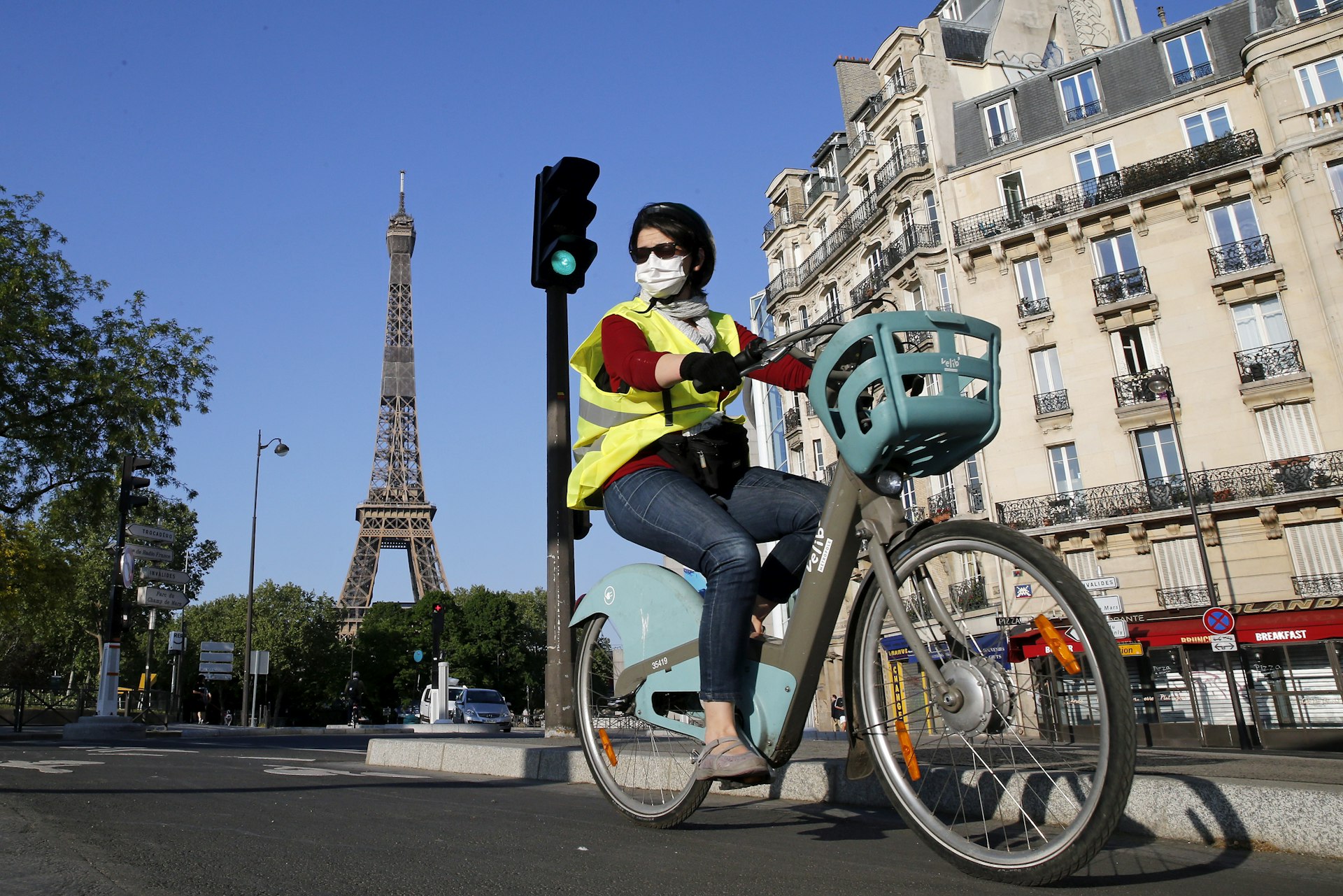A woman wearing a protective mask rides her bicycle next to the Eiffel Tower as the lockdown continues due to the coronavirus outbreak (COVID 19) on April 23, 2020 in Paris, France.