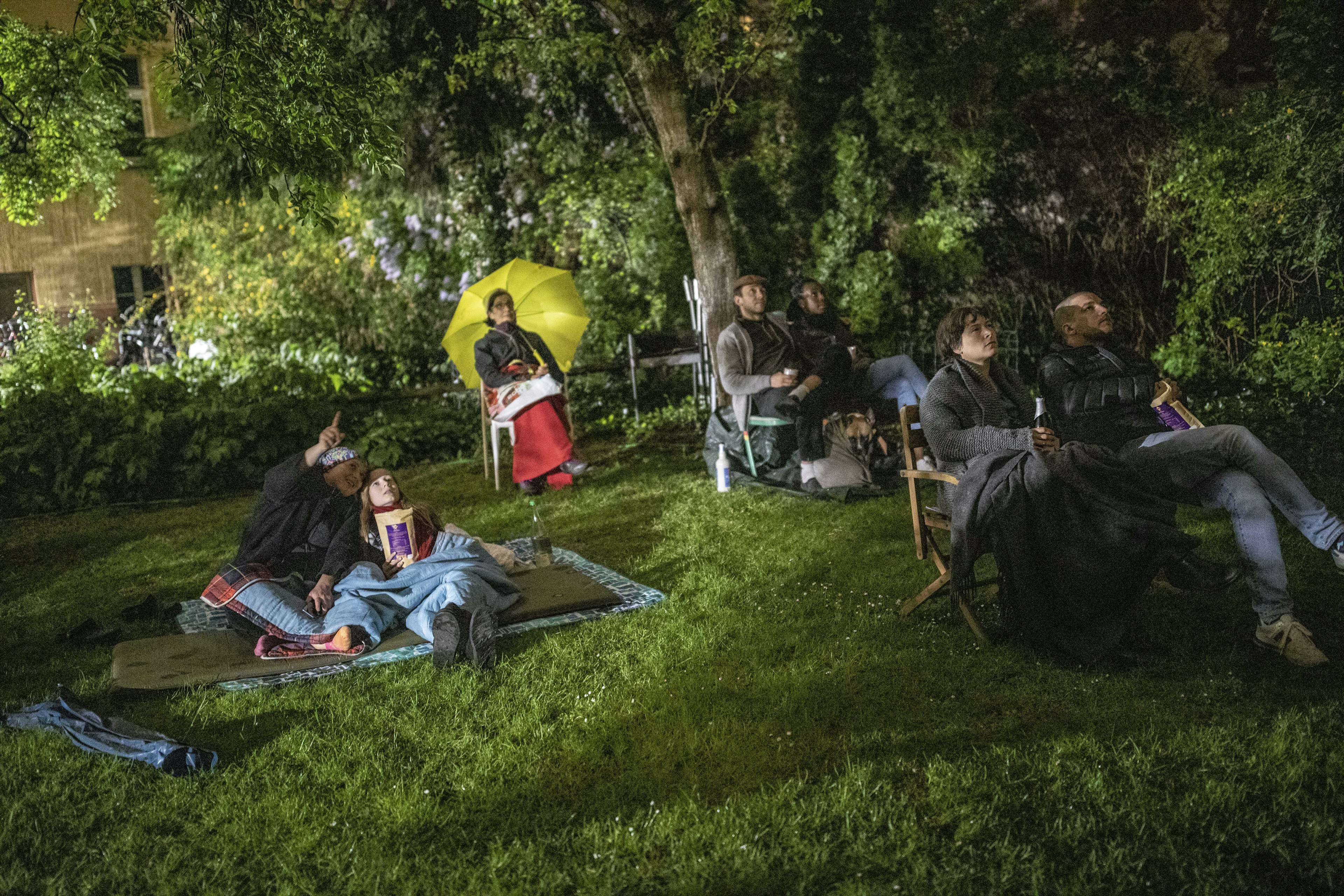 Residents gather in a courtyard to watch a movie projected on the backyard firewall of residential building