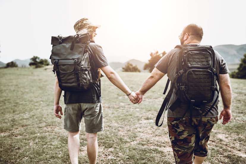 Gay Couple Walking Towards Sunset On Hill While hiking