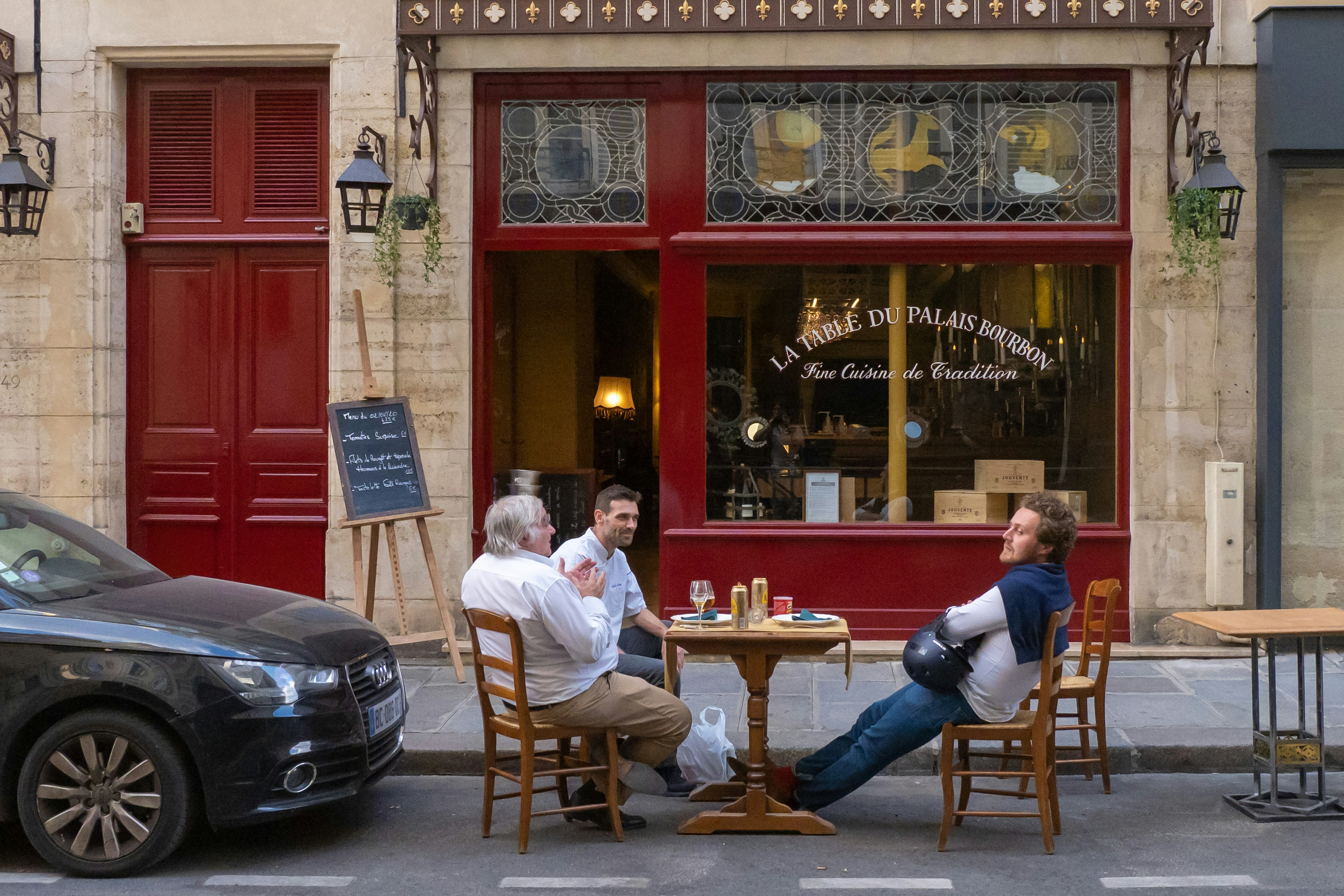 People sit at a terrace on street parking lots between cars