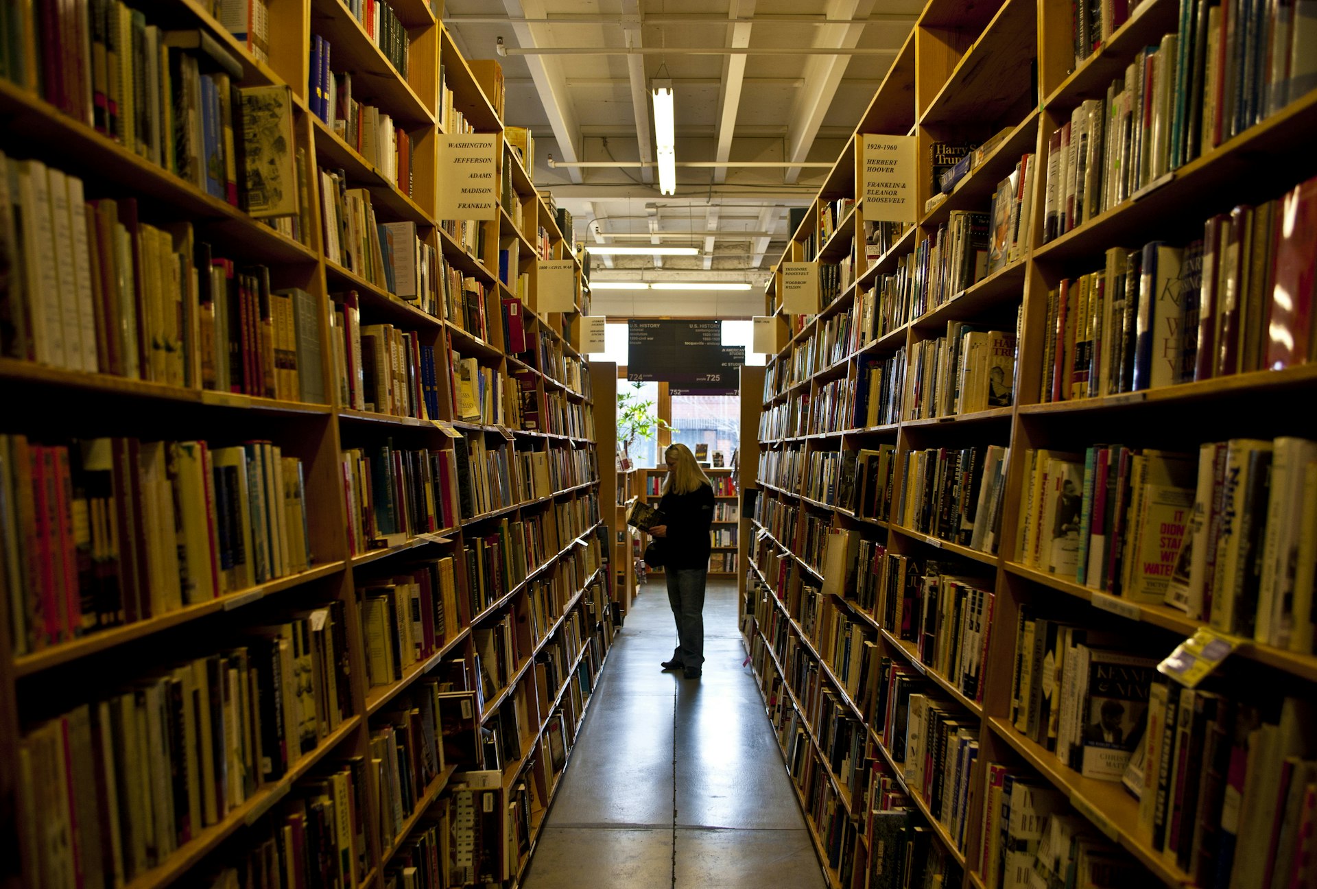 A woman peeks into a book at the end of a long row of bookshelves on the ground floor of Powell's City of Books in Portland, Oregon