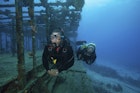 Two divers swimming along the remaining structure of a shipwreck.