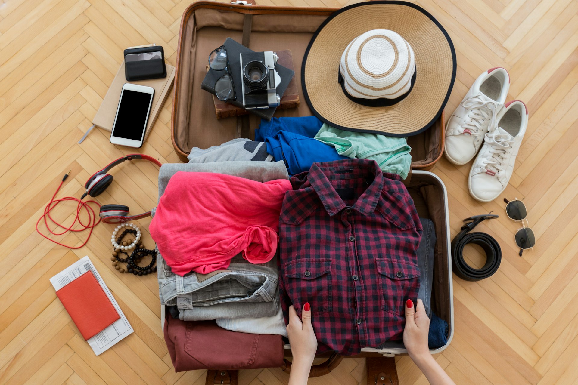 Woman hand preparing summer luggage. A phone, a hat and clothes are in her suitcase.