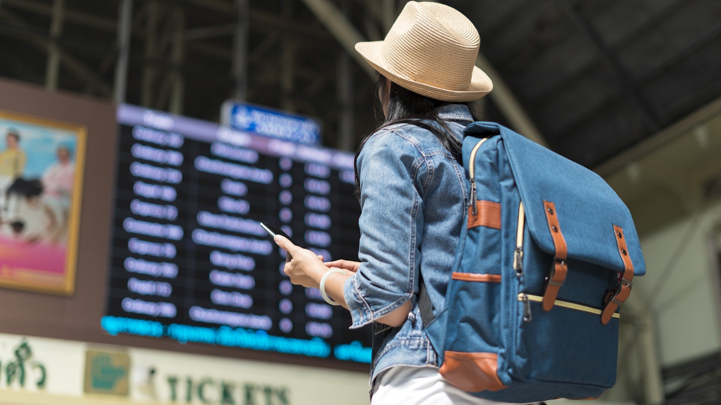 Young female backpacker checking her train arrival on a digital timetable board.