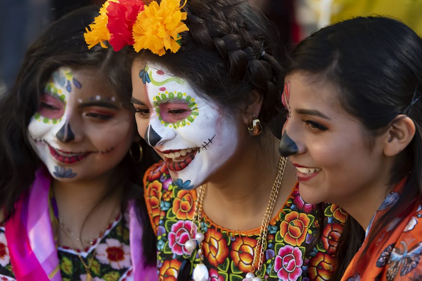 Tre flickor i traditionella kläder, en med ansiktsfärgad skalle, på Día de los Muertos-festivalen i Oaxaca