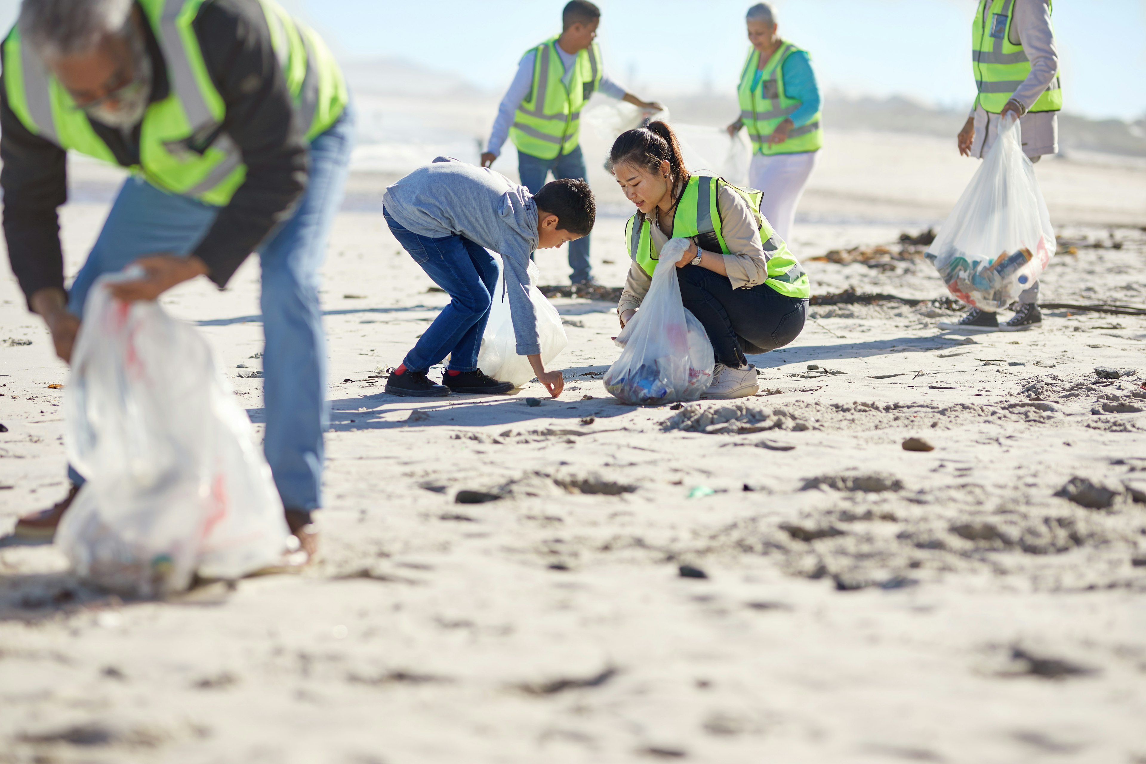 Mother and son with other volunteers cleaning up litter on a sunny, sandy beach.