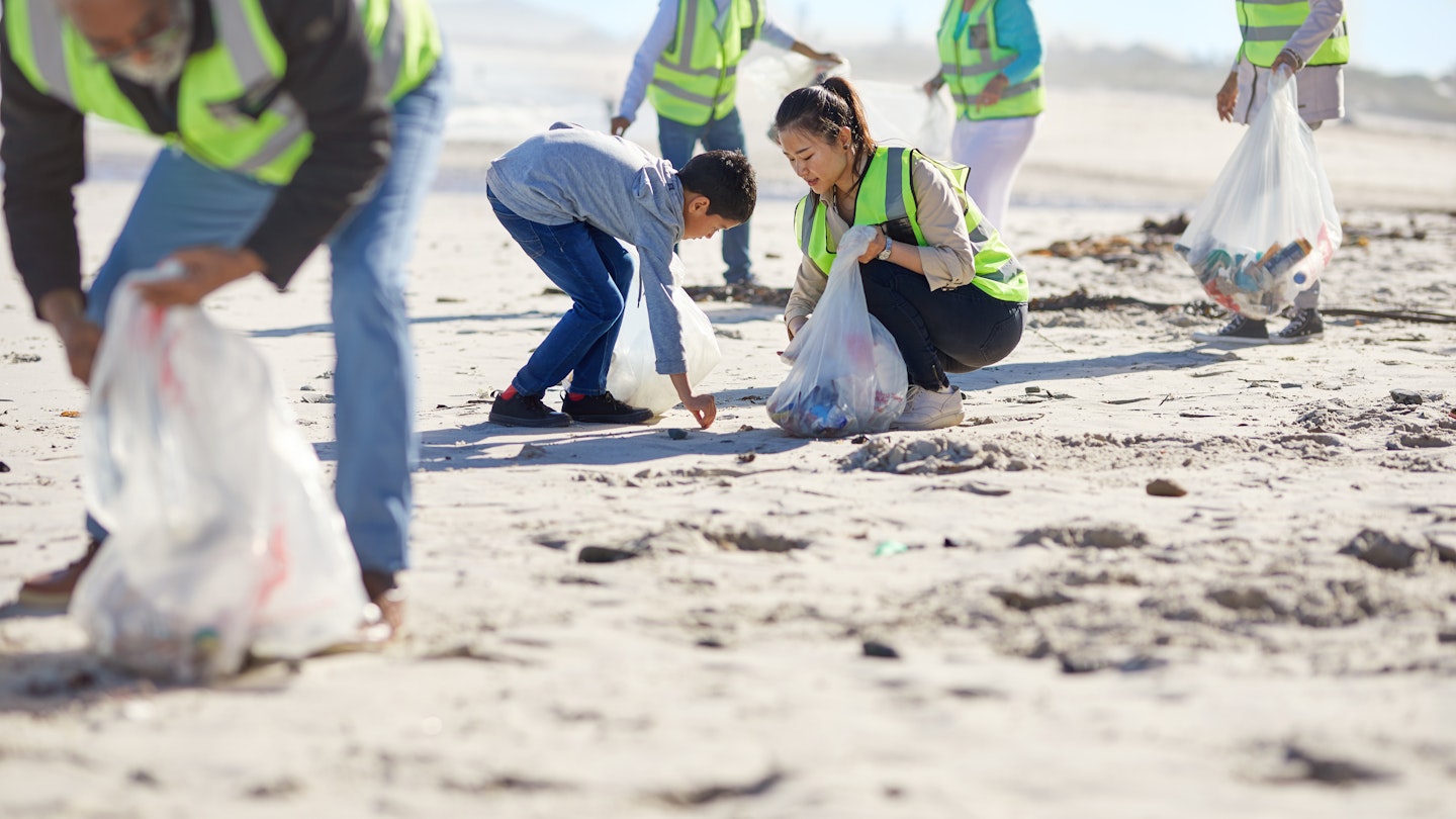 Mother and son with other volunteers cleaning up litter on a sunny, sandy beach.