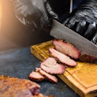 Culinary master class: A chef wearing black cooking gloves slices smoked beef brisket with a knife.