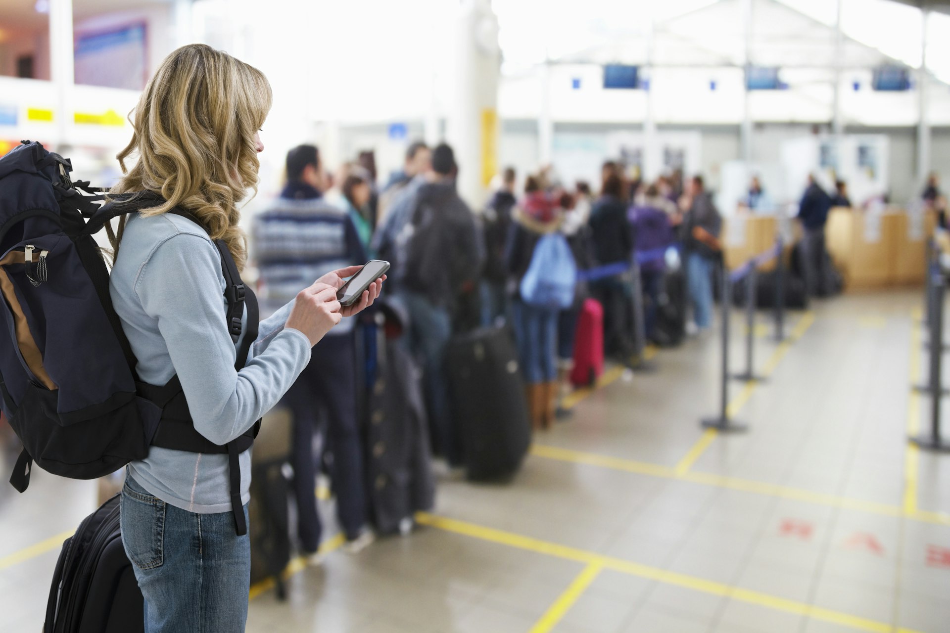 A woman waits in a line to board a plane. She's playing with her phone