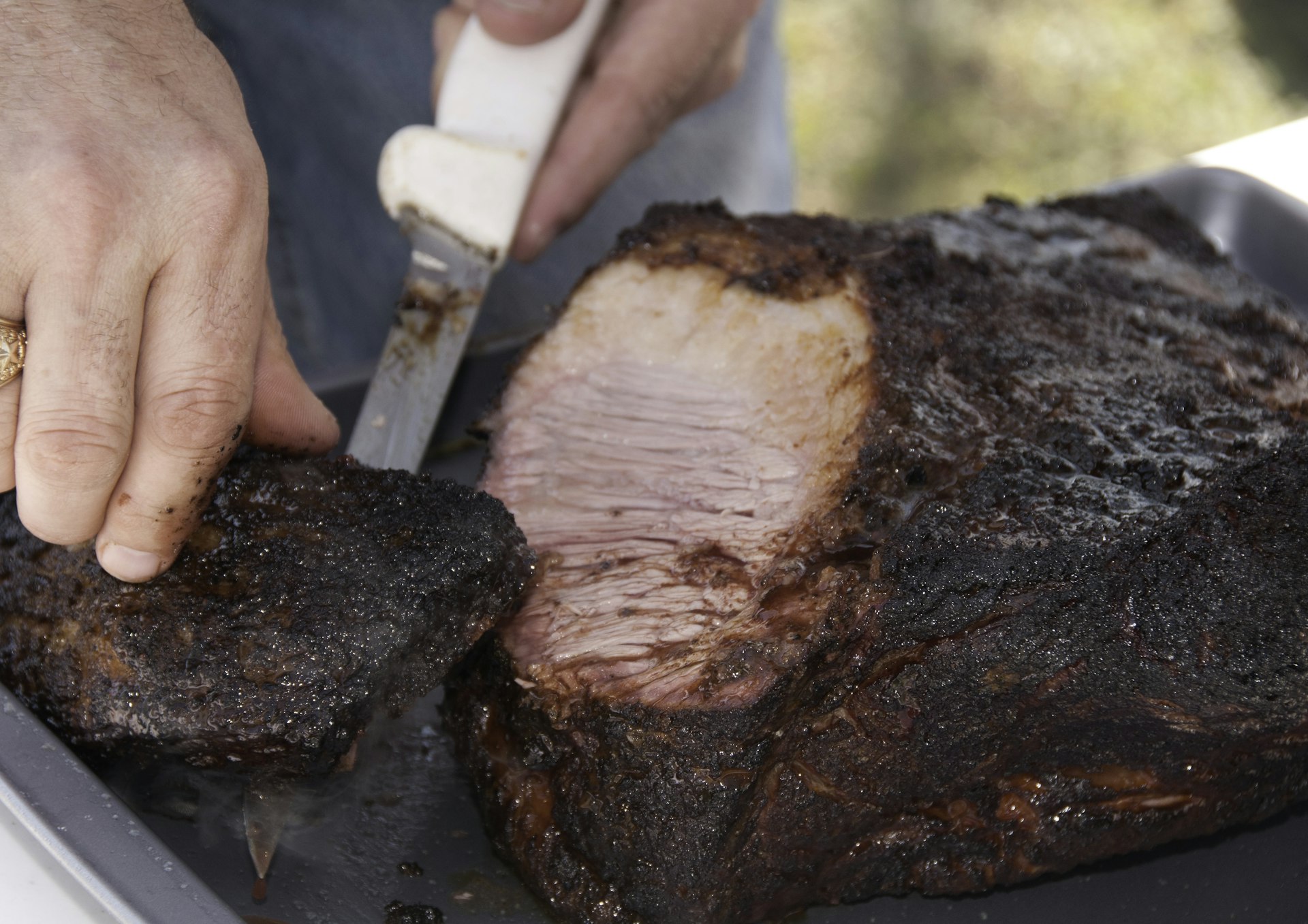 Man cutting smoked brisket on a metal pan