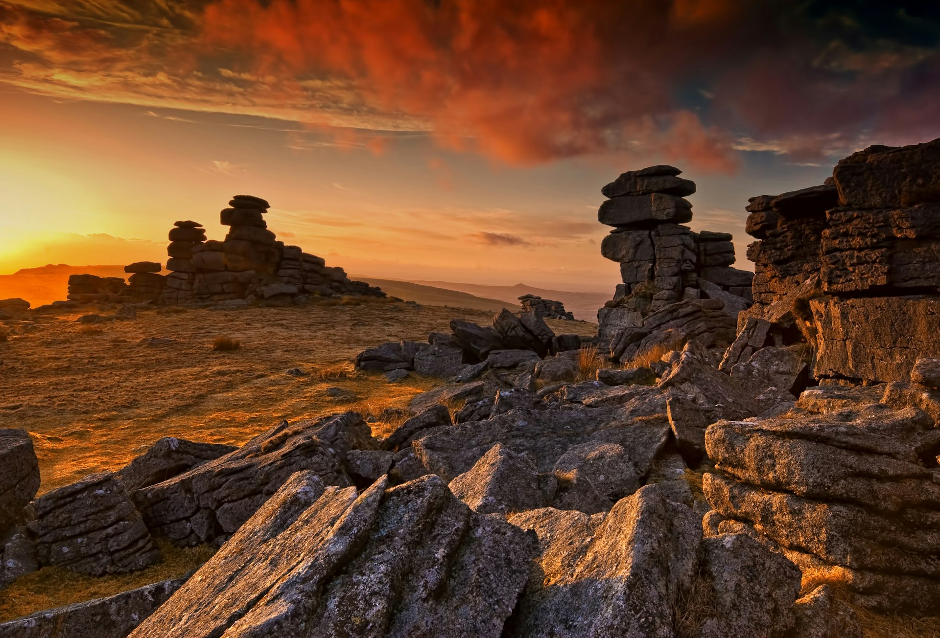The sun sets behind tors, large granite stacks of rocks, on deserted moorland