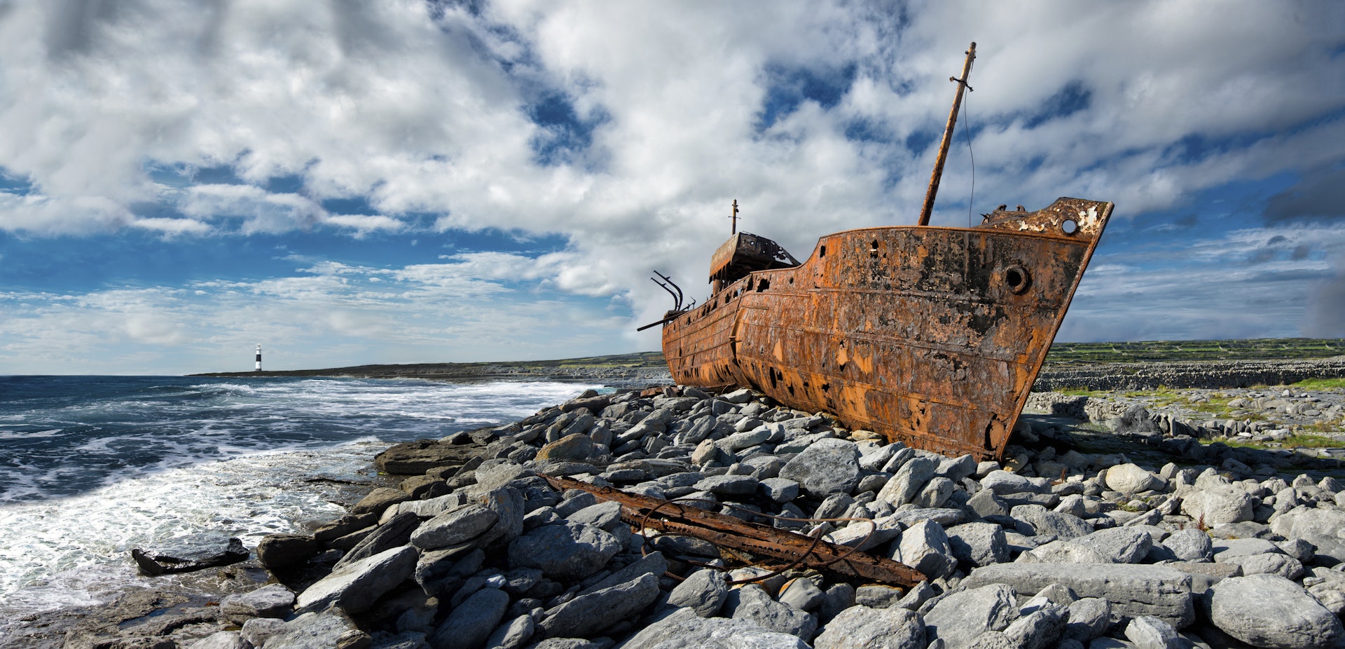 A rusted metal hull of a shipwrecked boat on a rocky shore
