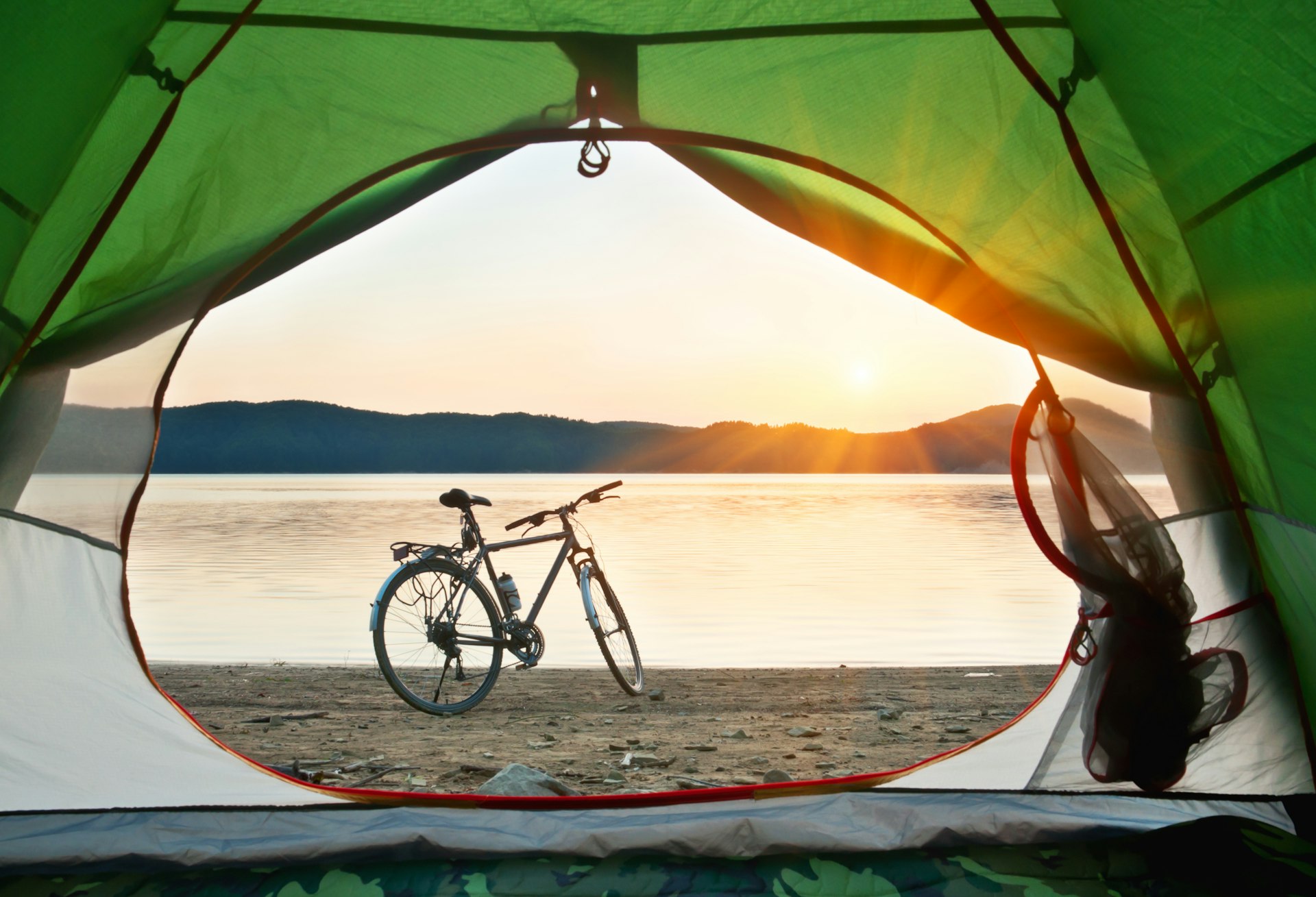 A bicycle on the shore of some water, viewed through the opening in a tent