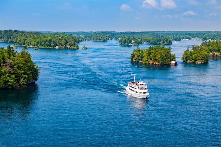Photo taken from above of a tour boat with tourists passing between islands in Thousand Islands National Park, St. Lawrence River, between Ontario, Canada and New York State, USA.