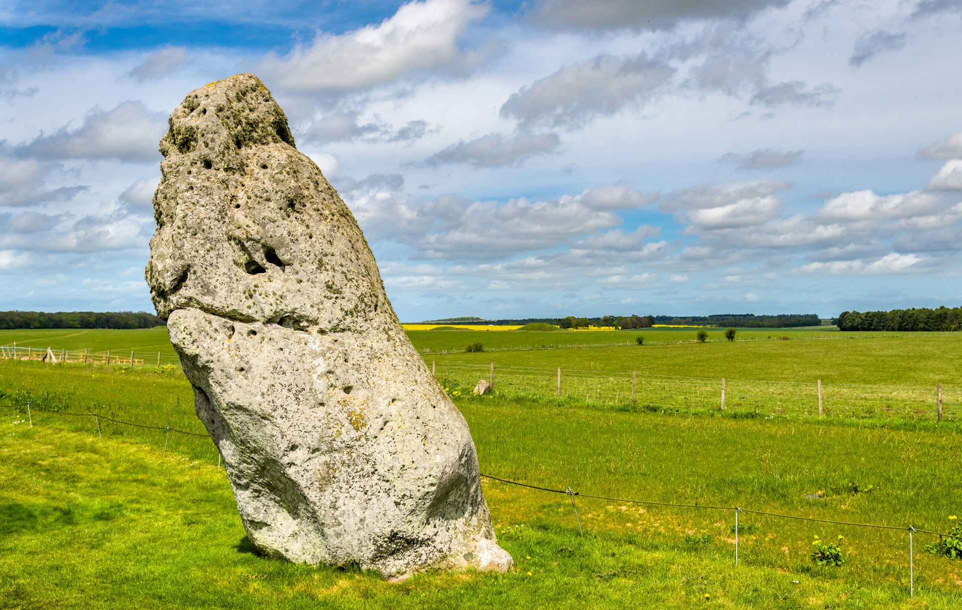 A giant stone stands alone, surrounded by green farmland. The stone leans slightly to the left