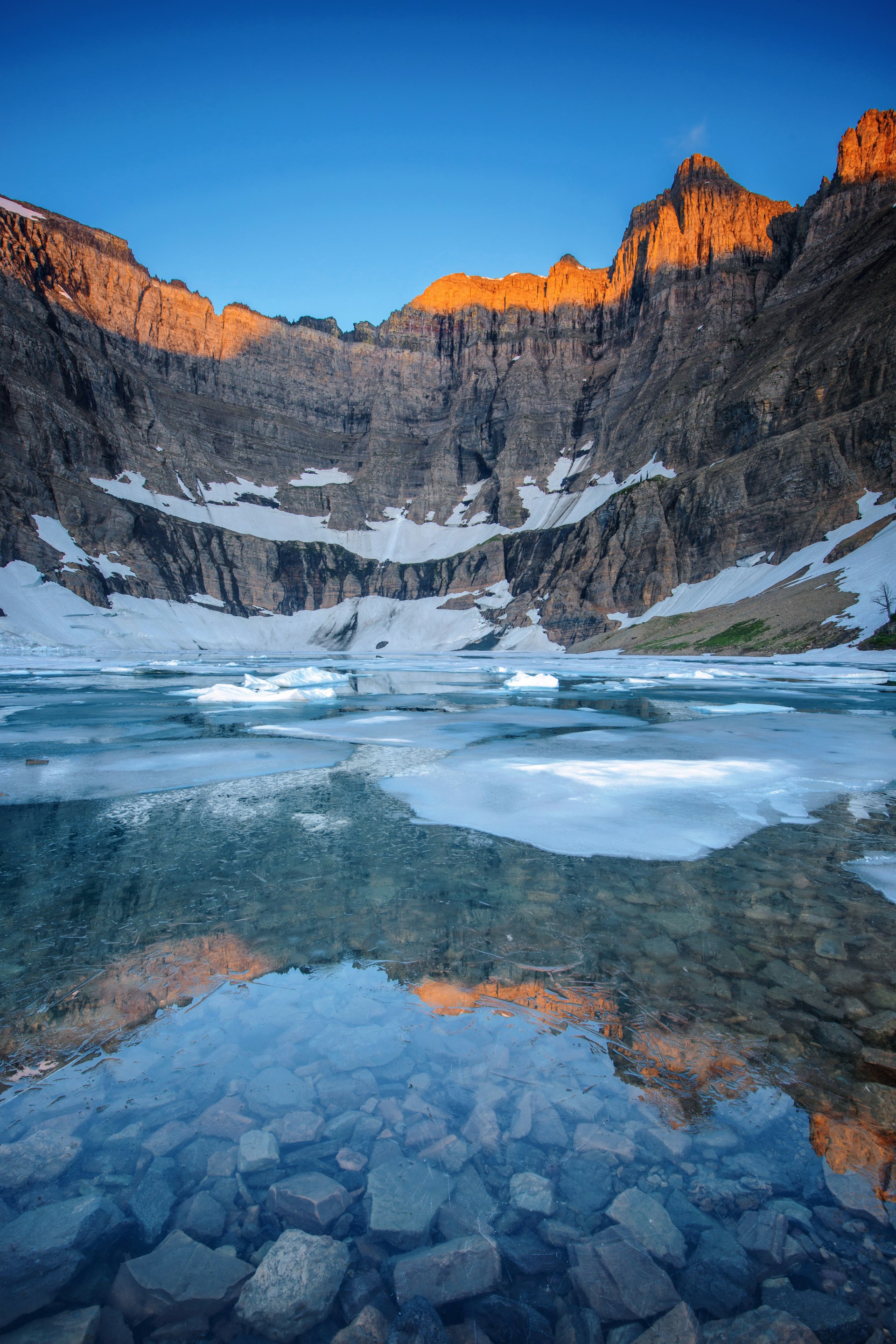 The sun kisses the top of jagged mountain peaks as it rises. The lake is crystal clear