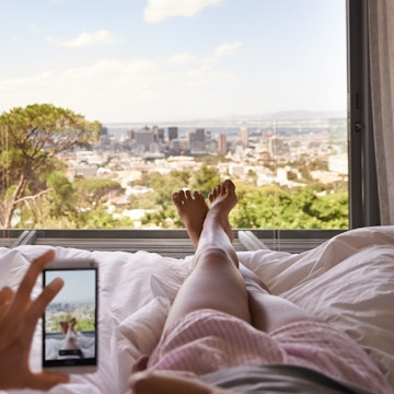 Cropped shot of a woman in bed taking a picture of the view from her bedroom