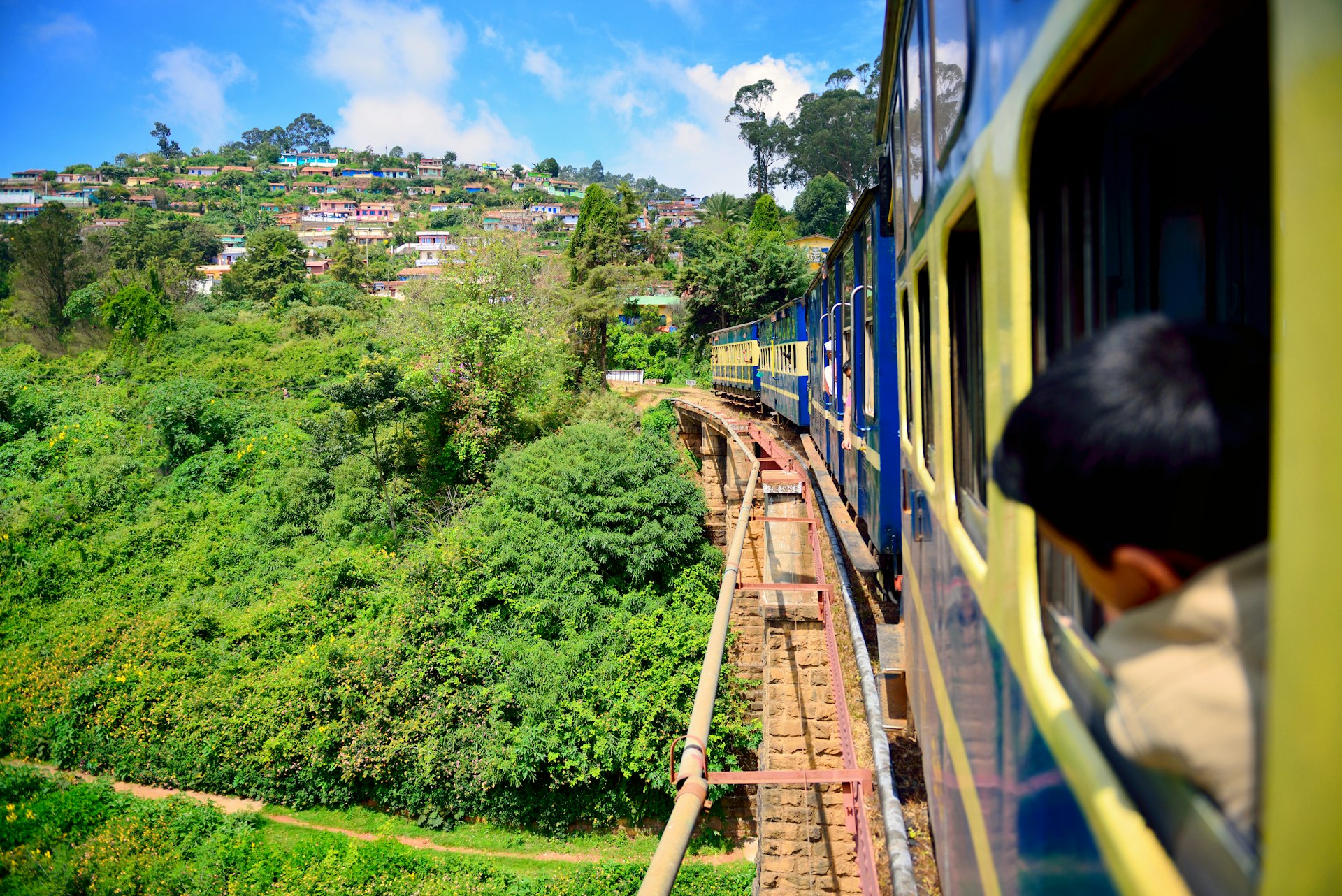 A train crossing a bridge curves through lush green hillsides in India