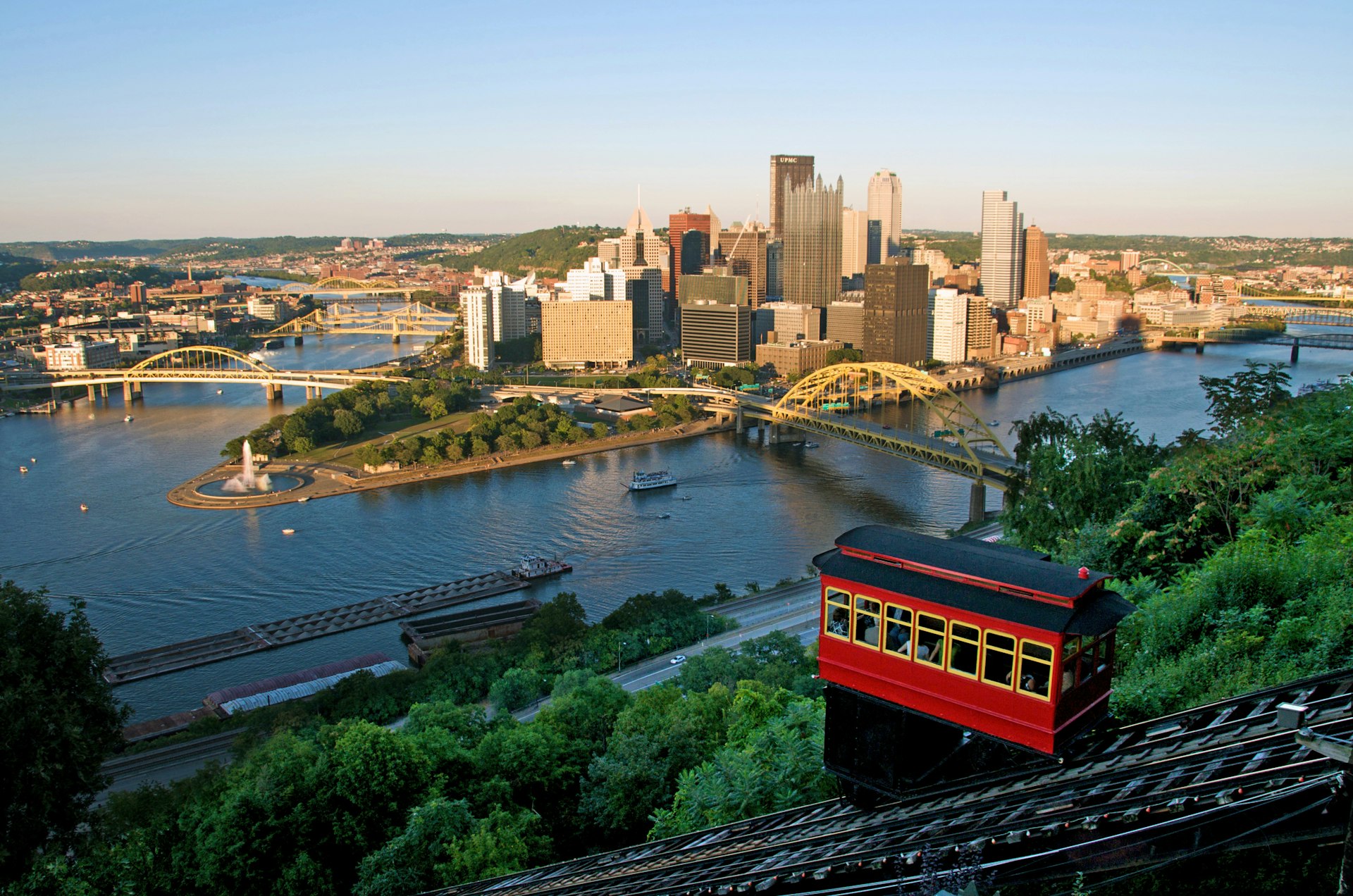 Pittsburgh skyline with high-rise buildings on an island between two rivers crossed by bridges. In the foreground is a red funicular carriage